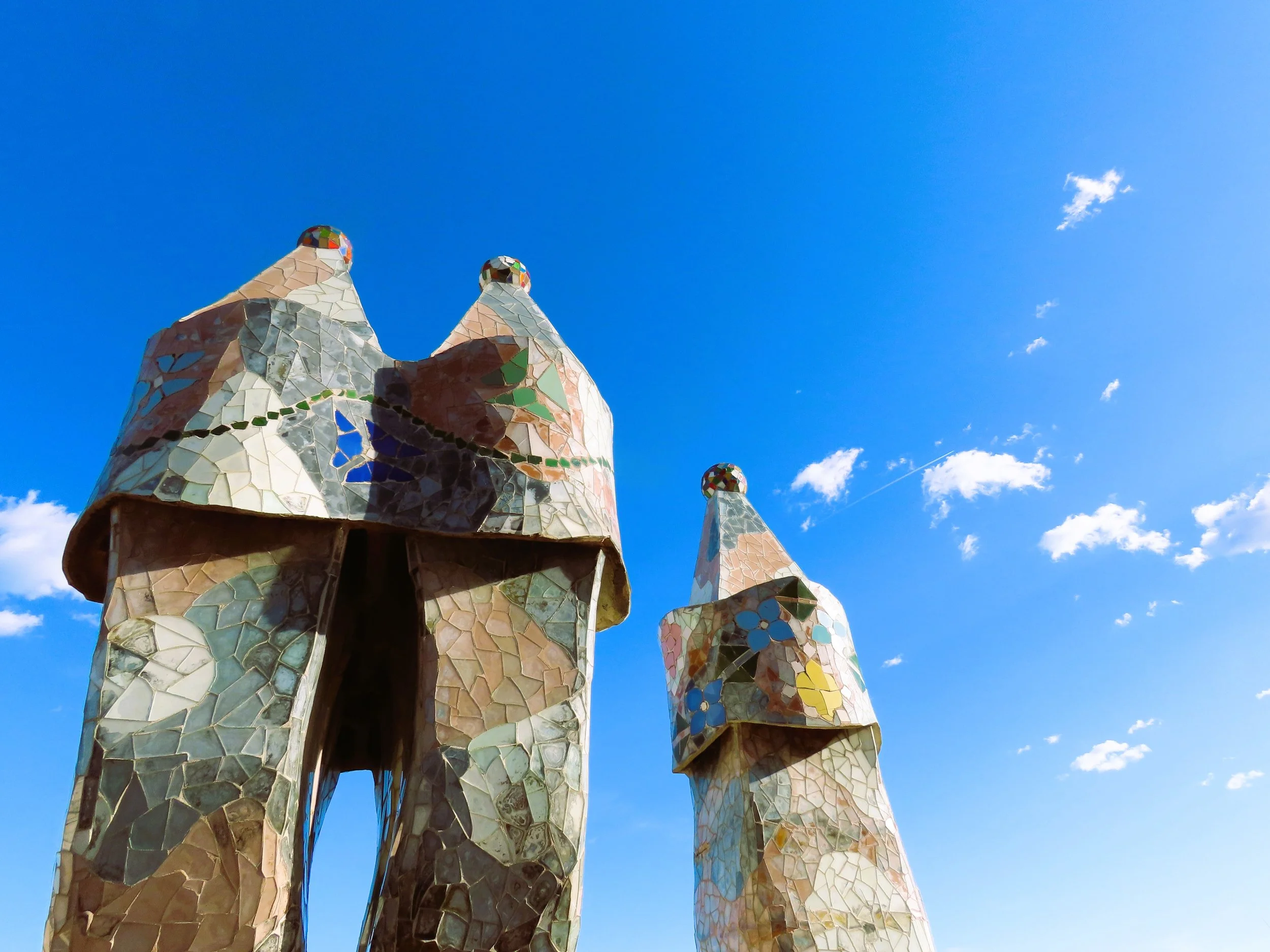 Due torri con facciate in mosaico di ceramica colorata, progettate da Antoni Gaudí, con un cielo azzurro e alcune nuvole.