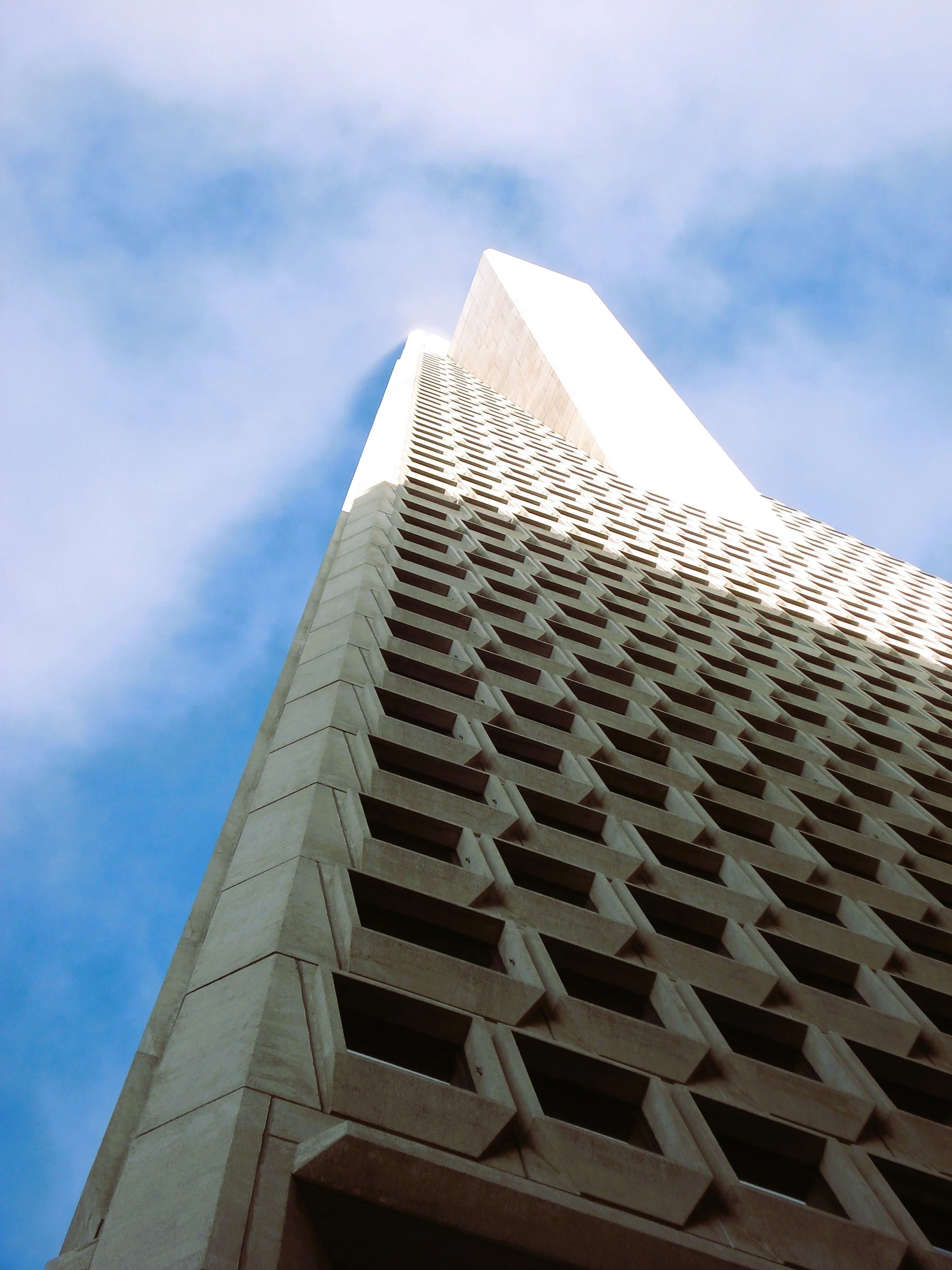 Impressionante vista di un grattacielo moderno visto dal basso, con un disegno architettonico unico e una facciata con aperture a forma di pentagono, contro un cielo azzurro con alcune nuvole.