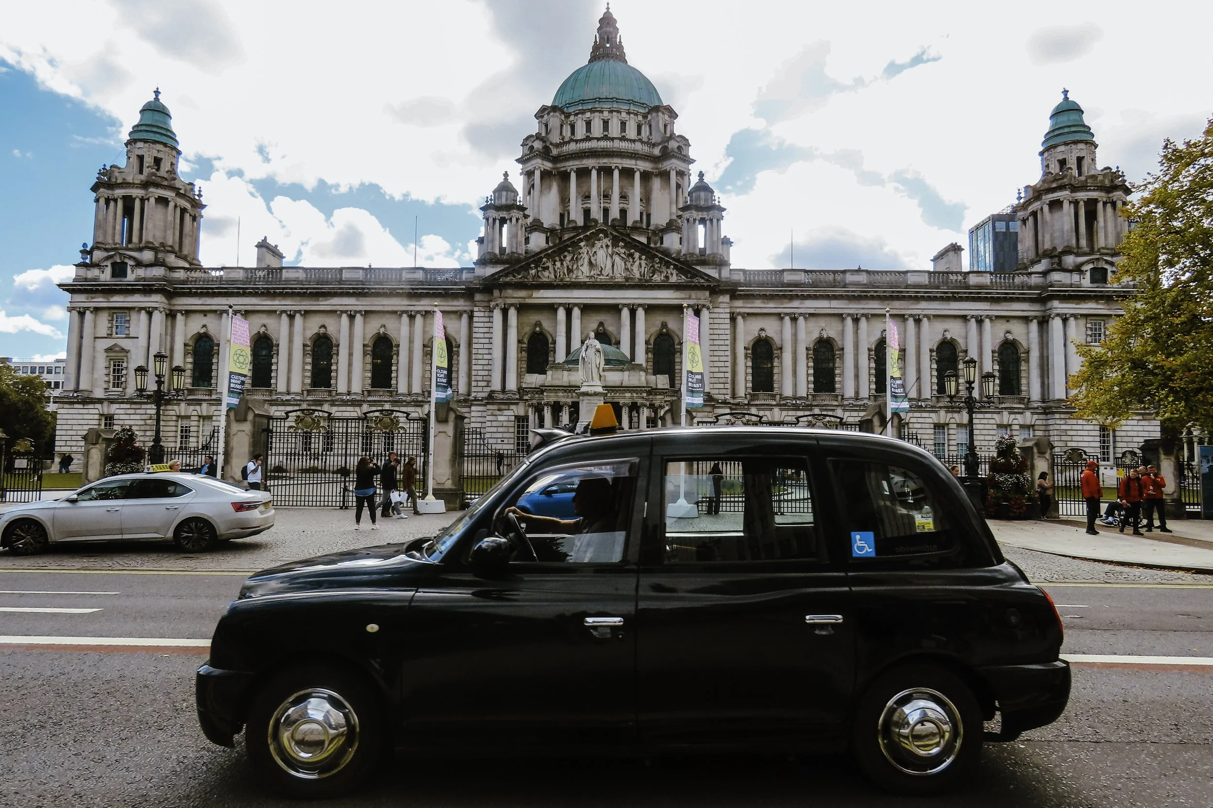 Un taxi nero che passa davanti al St. Paul's Cathedral a Londra, con persone che camminano e auto lungo la strada.
