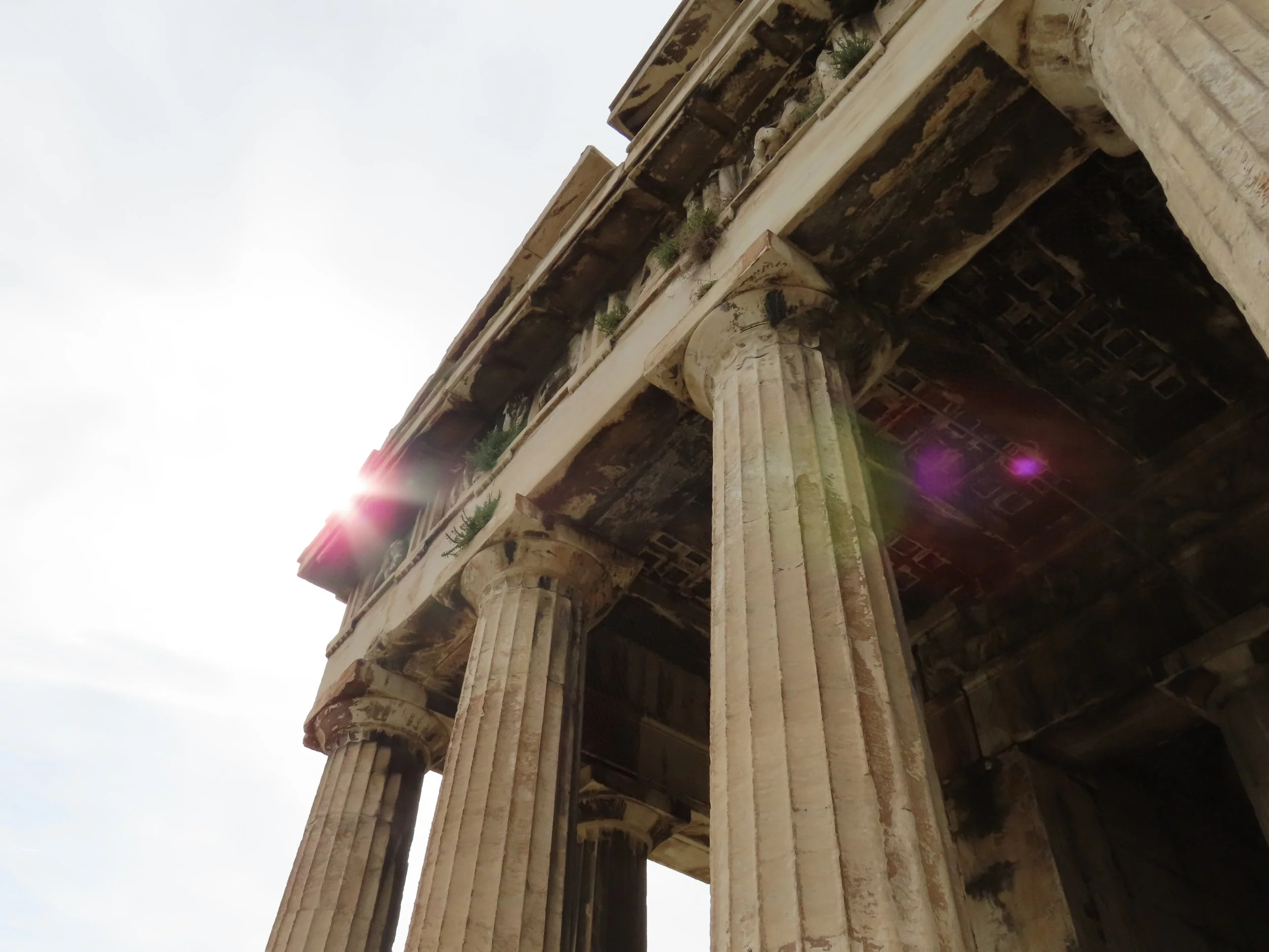 Colonne e parte del soffitto di un edificio antico, probabilmente un tempio greco, con il sole che splende dietro di esso.