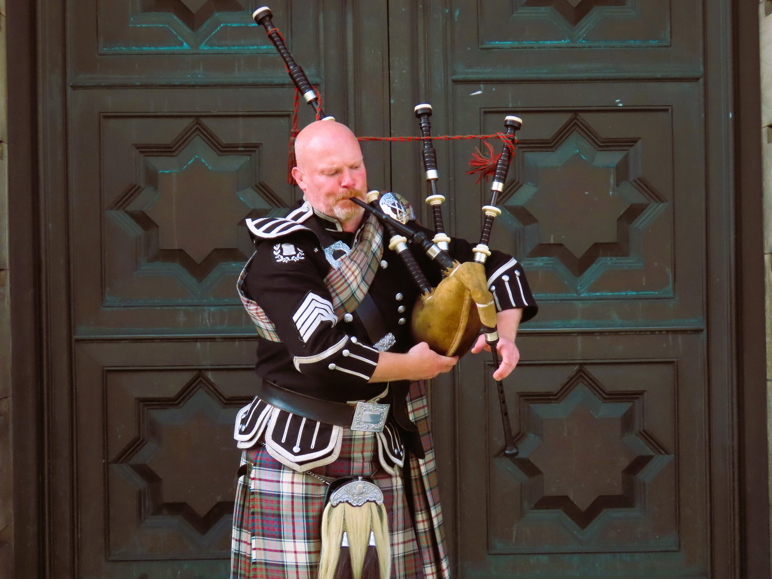 Un uomo che suona le cornamuse in costume tradizionale davanti a una porta di legno.