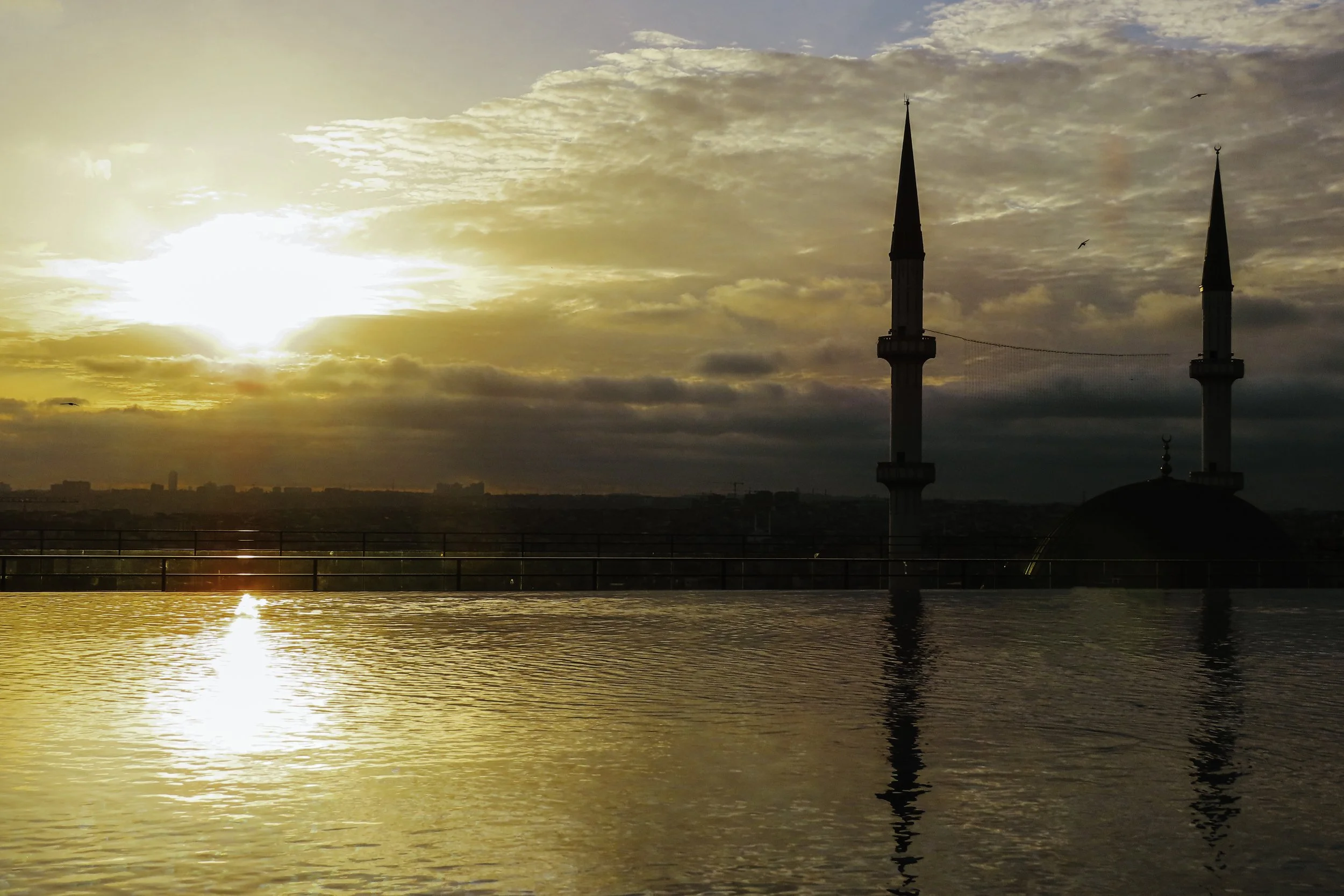 Alba al tramonto con due minareti di una moschea in silhouette e riflesso sull'acqua