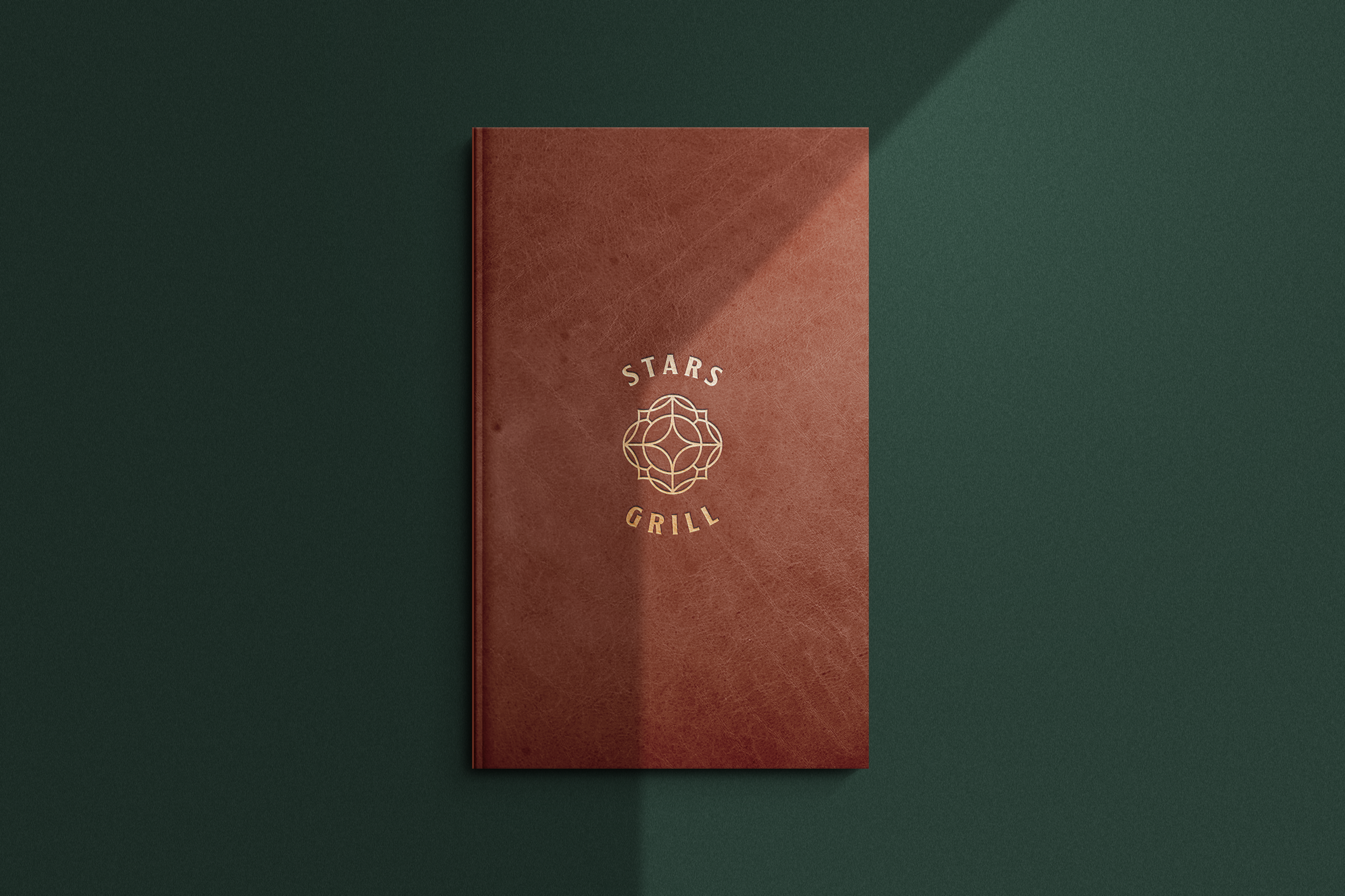 A brown leather book with a geometric logo and the words 'Stars Grill' on the cover, placed on a dark green surface with a shadow cast to the upper right.