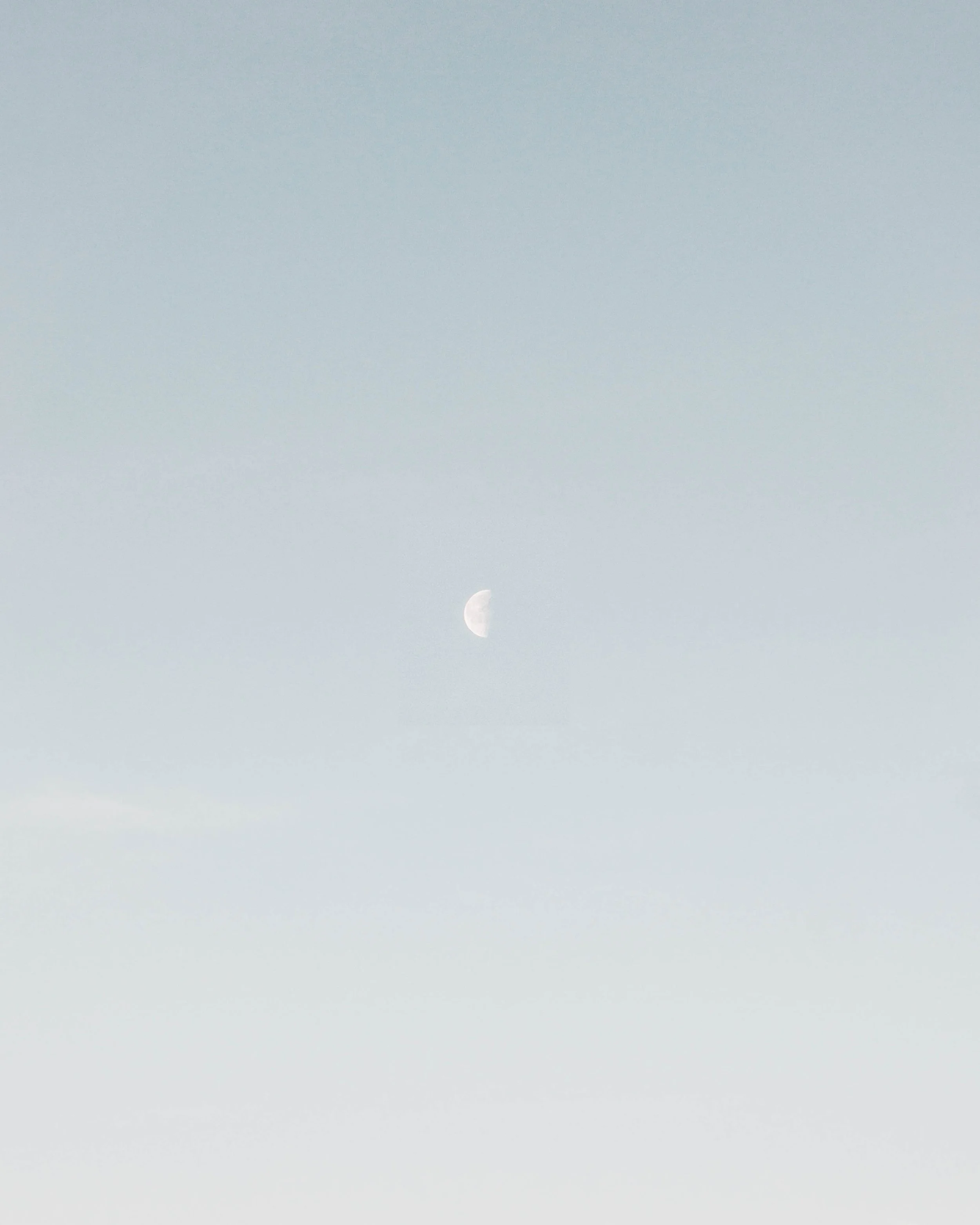 A sky with a visible moon near the horizon during daytime or early evening.