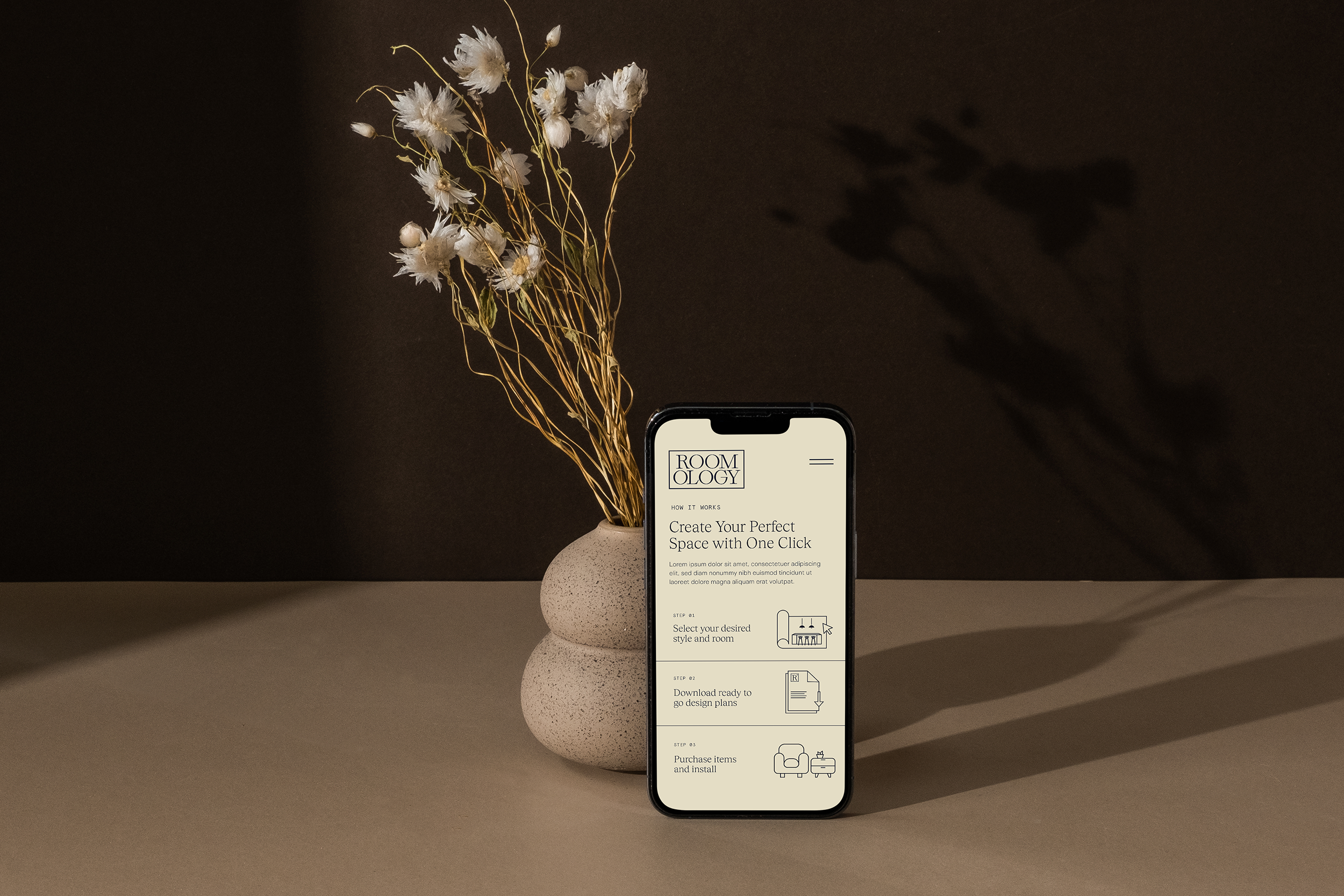 A smartphone displaying a web page about creating perfect space with one click, with a dried flower arrangement in a beige vase in the background.