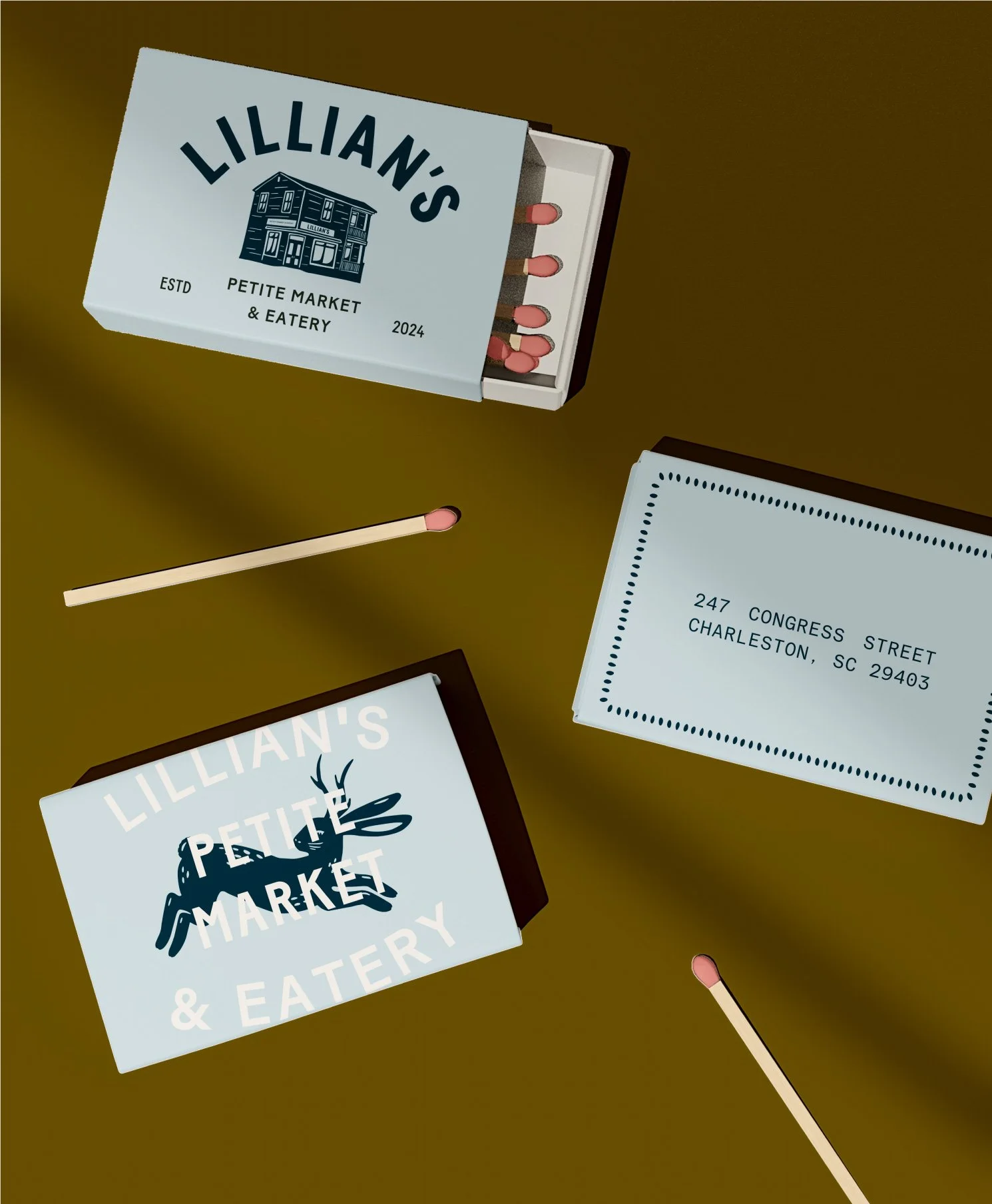 A box labeled 'Lillian's Petite Market & Eatery' contains pink-tipped matchsticks. Nearby, there is a postcard with the address 247 Congress Street, Charleston, SC 29403.