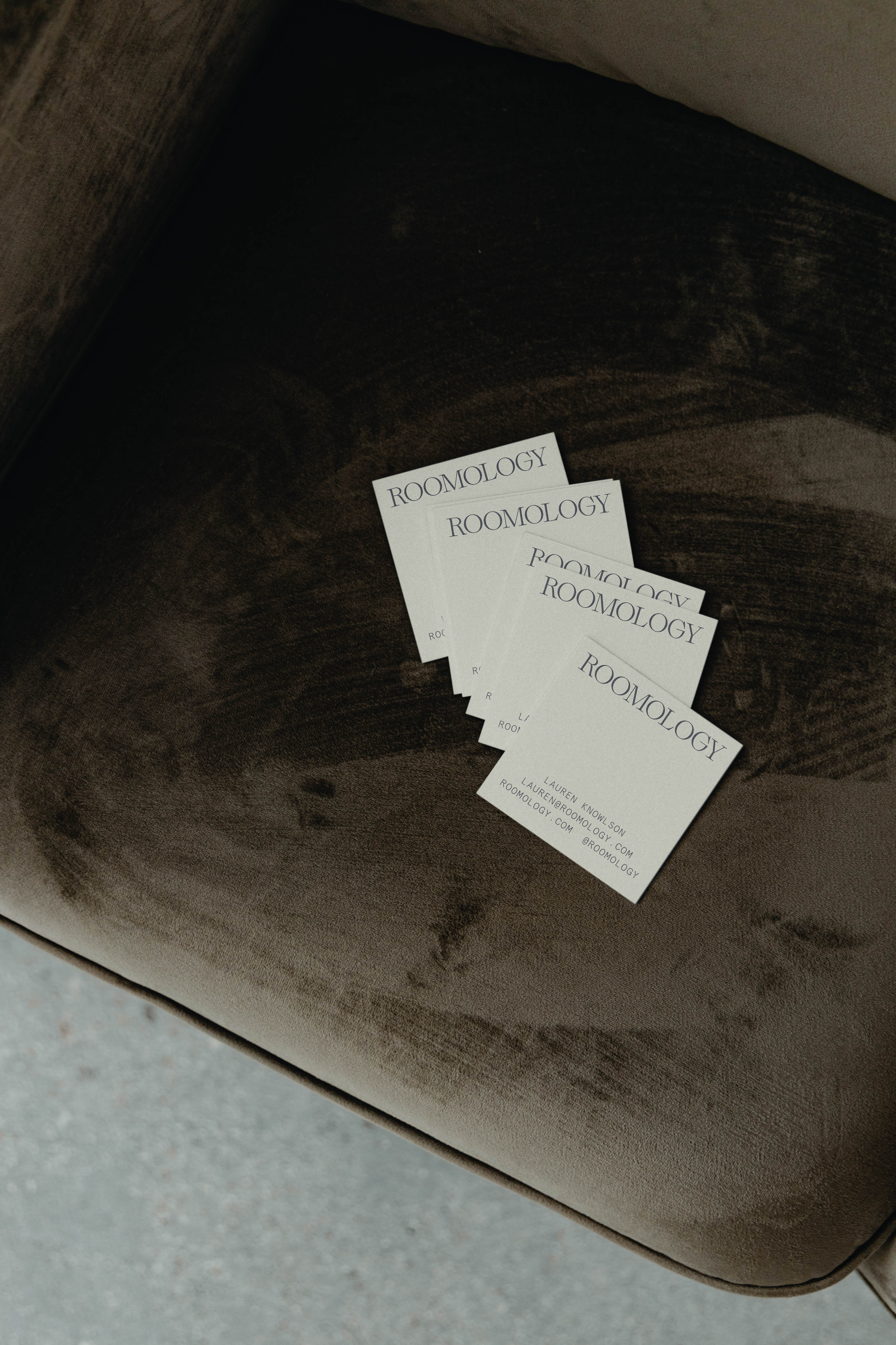 A dark-colored armchair with four business cards that say 'Roomology' on their surface.