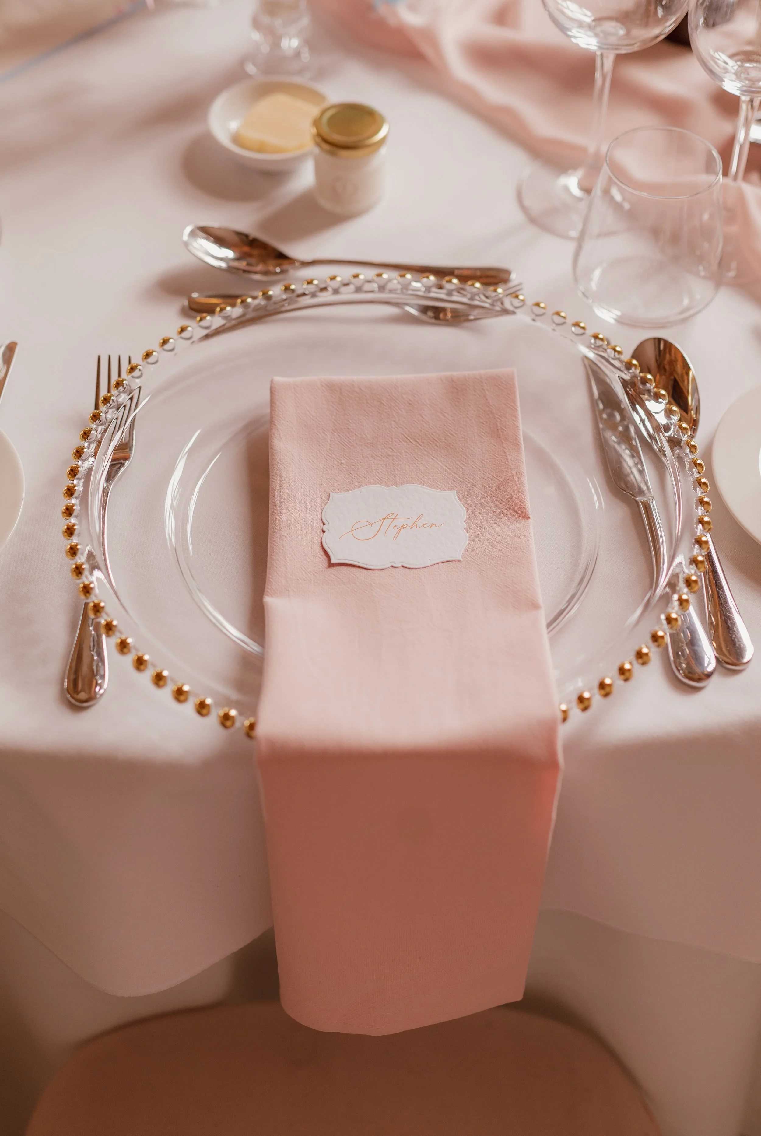 Pale pink stonewashed cotton napkin with a scalloped place card on a gold-beaded glass charger at Ashridge House.