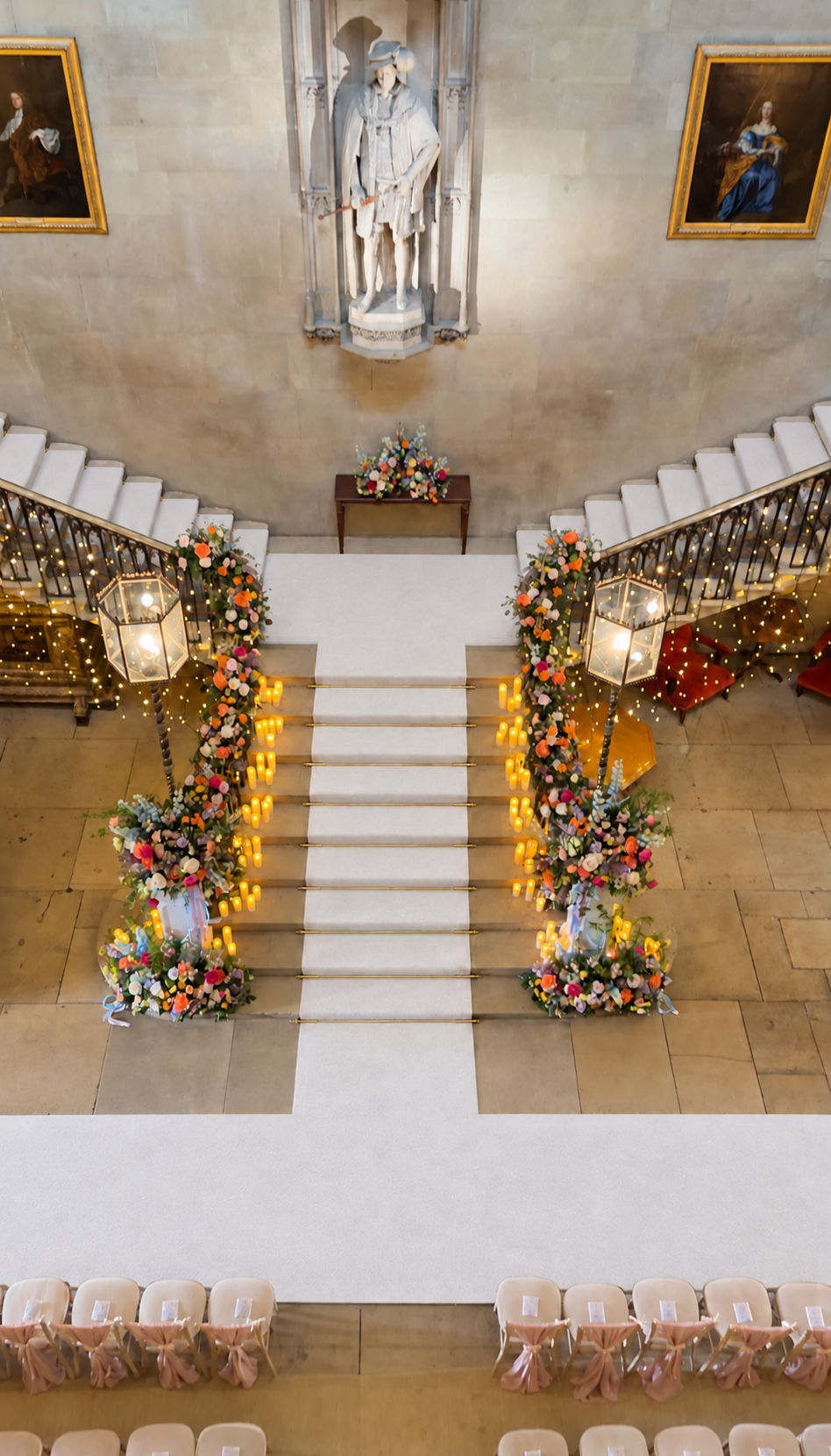 White wedding carpet runner on Ashridge House’s Grand Staircase, with brass stair rods, white flowers, greenery and warm fairy lights.