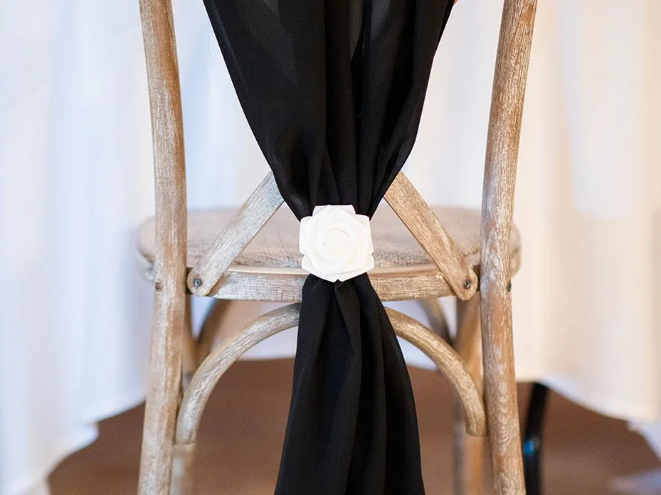 Black chair drape with white rose embellishment by Rosewood & Pearl