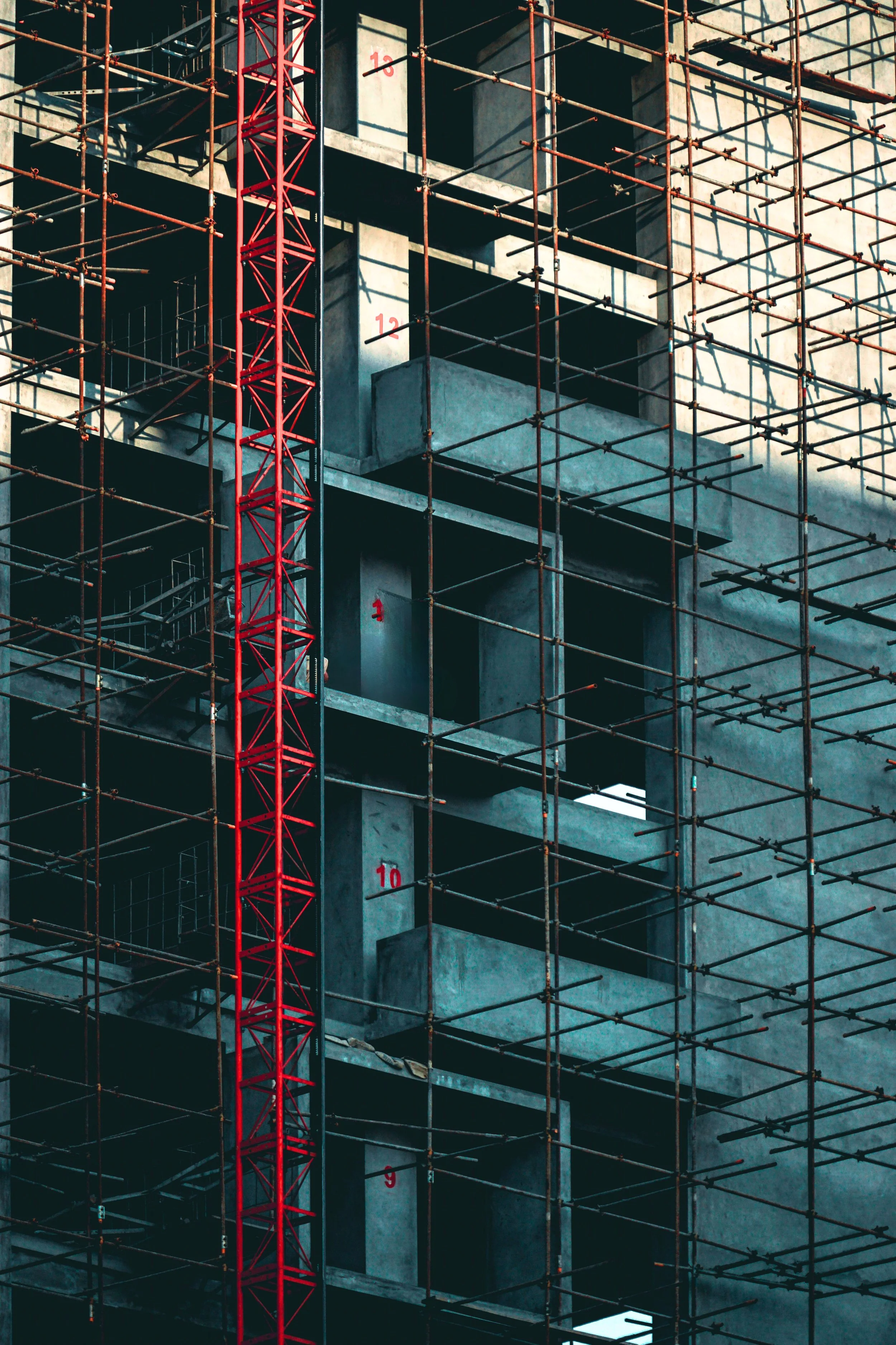 Construction site with a multi-story building under construction, featuring concrete floors and walls, surrounded by scaffolding and a red construction crane.