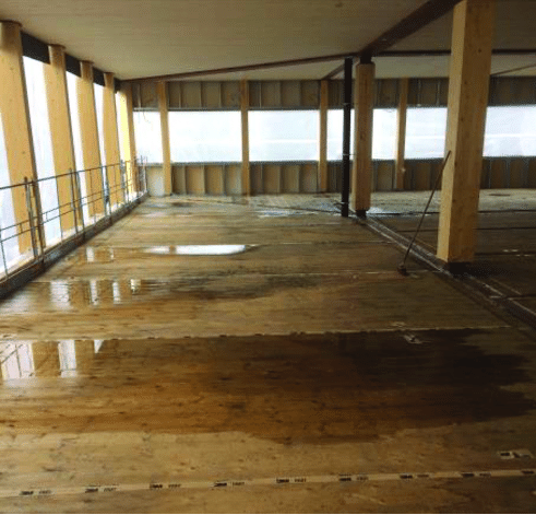 Indoor construction site with wooden floors and unfinished walls, with large windows and support beams. Showing water and condensation accumulation on a construction site, something that Climate Control Canada helps prevent with our expertise.