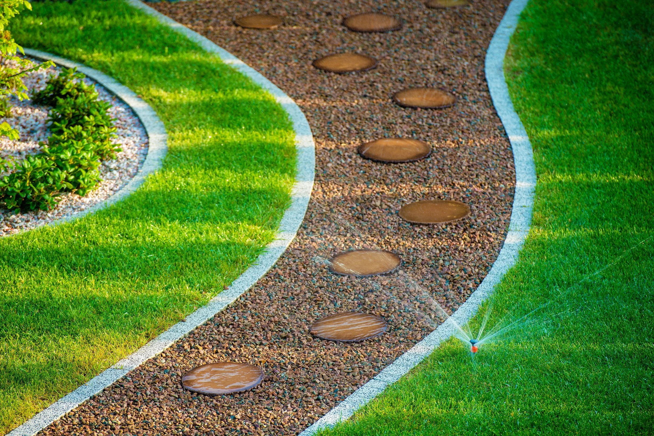Garden pathway with stepping stones and a sprinkler watering the grass.