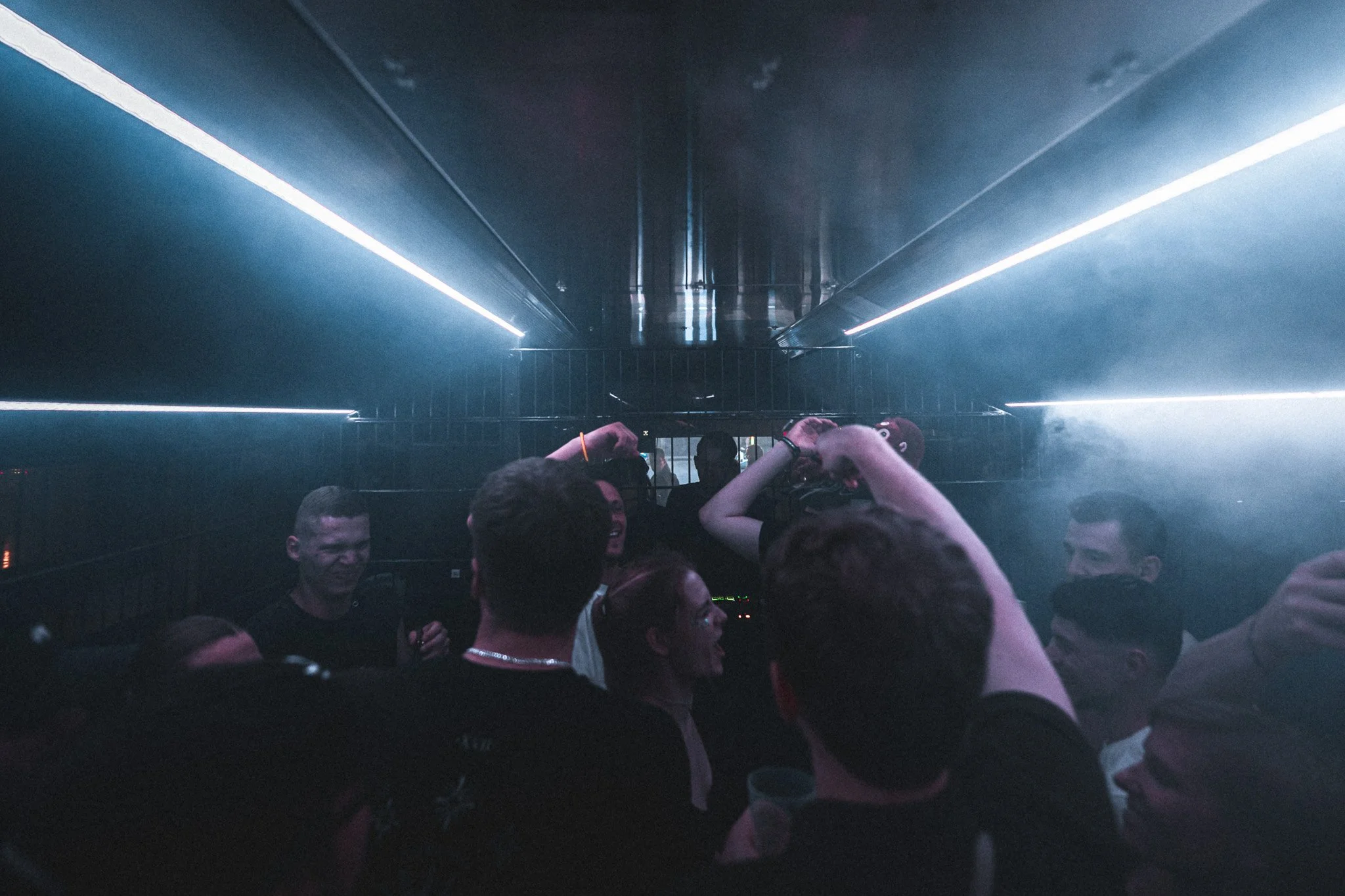 People dancing and enjoying a nightclub with blue lighting and fog.