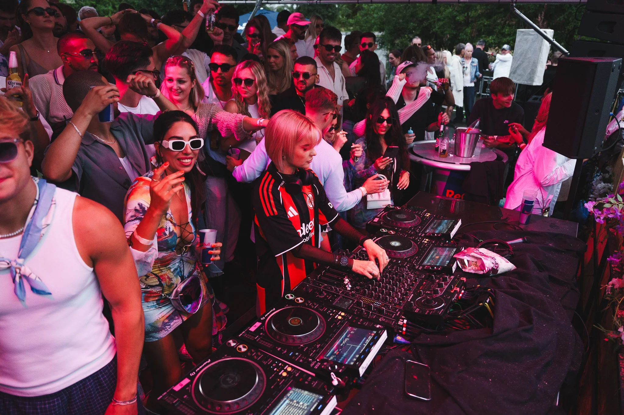 Crowd of people dancing and enjoying a DJ at an outdoor party with DJ equipment in the foreground.