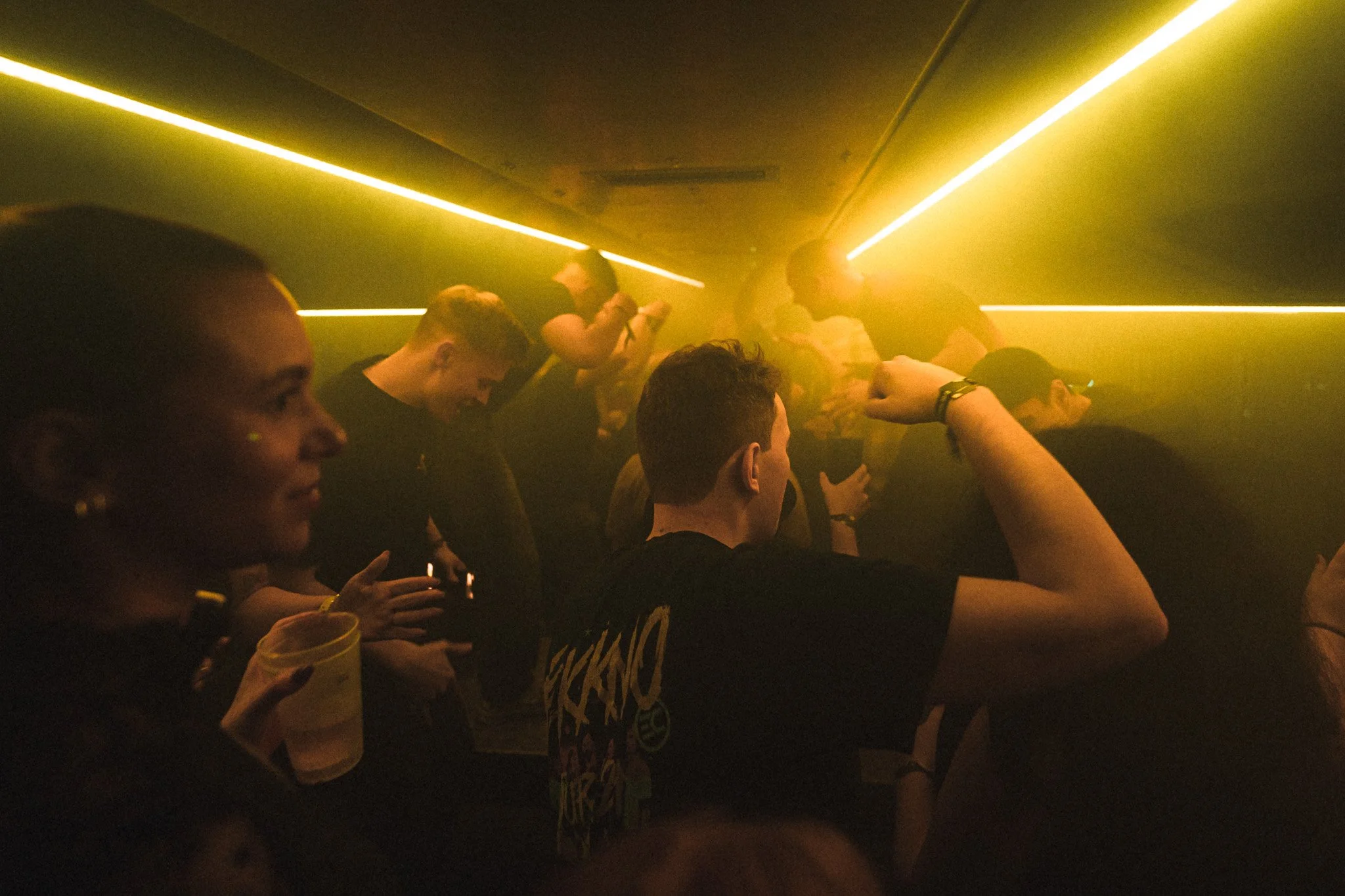 People dancing and enjoying a party with yellow lighting in a nightclub.