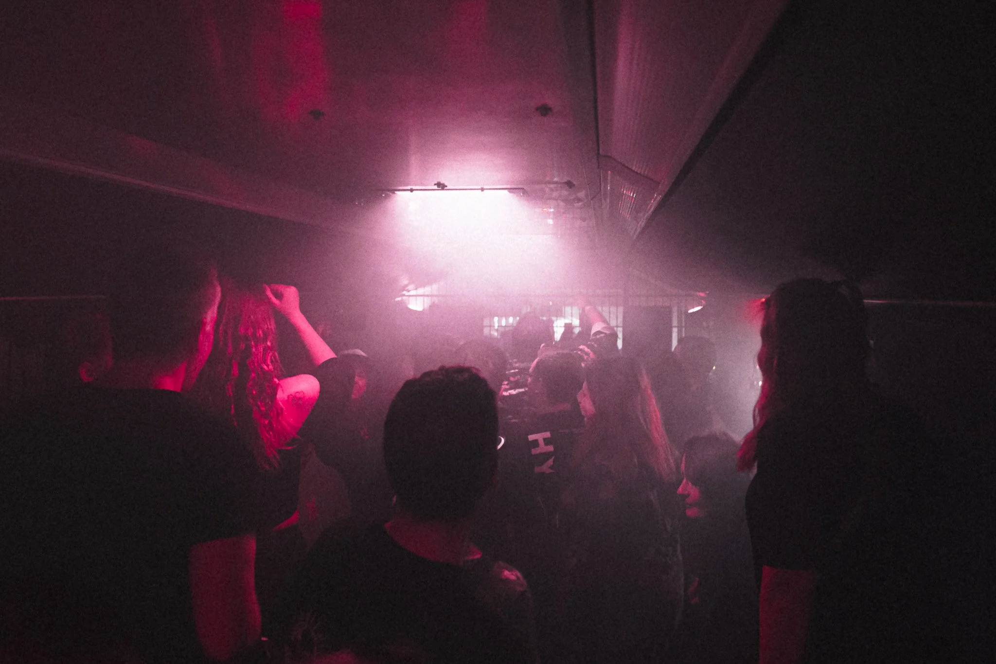 People dancing and socializing in a dimly lit nightclub with pink and purple lights.
