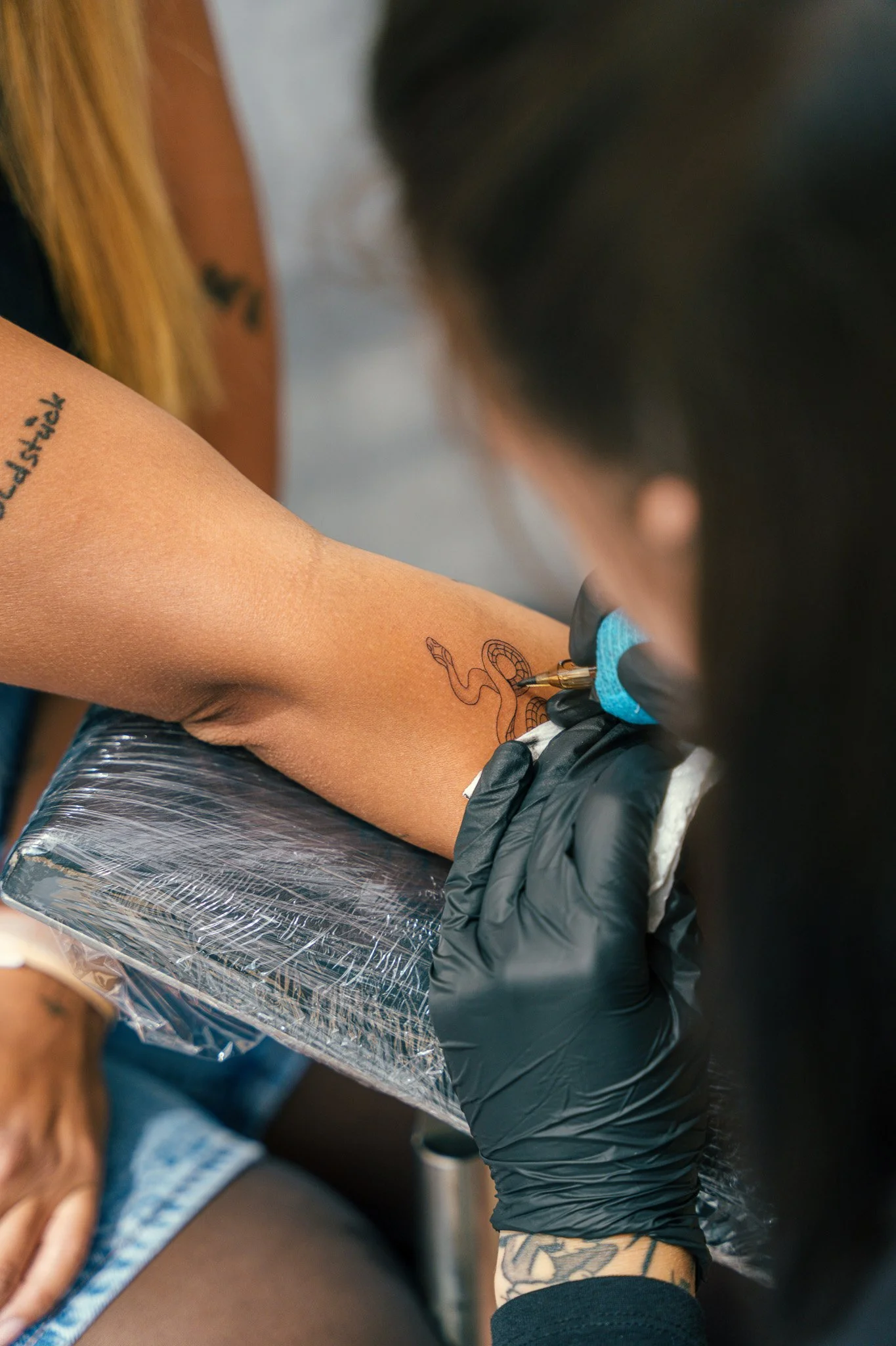 A tattoo artist is inkling a snake tattoo on a person's forearm.