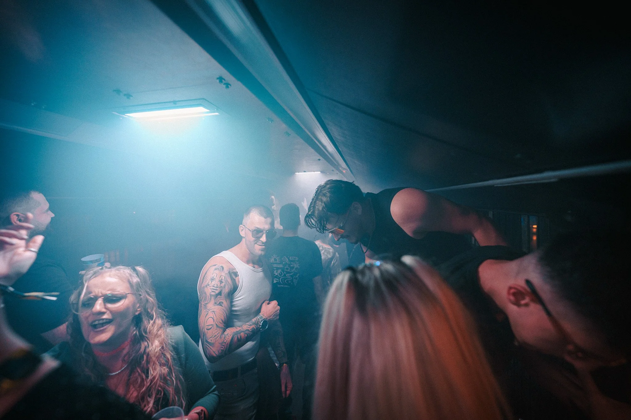 People dancing and socializing in a nightclub with colorful lighting and smoke effects.