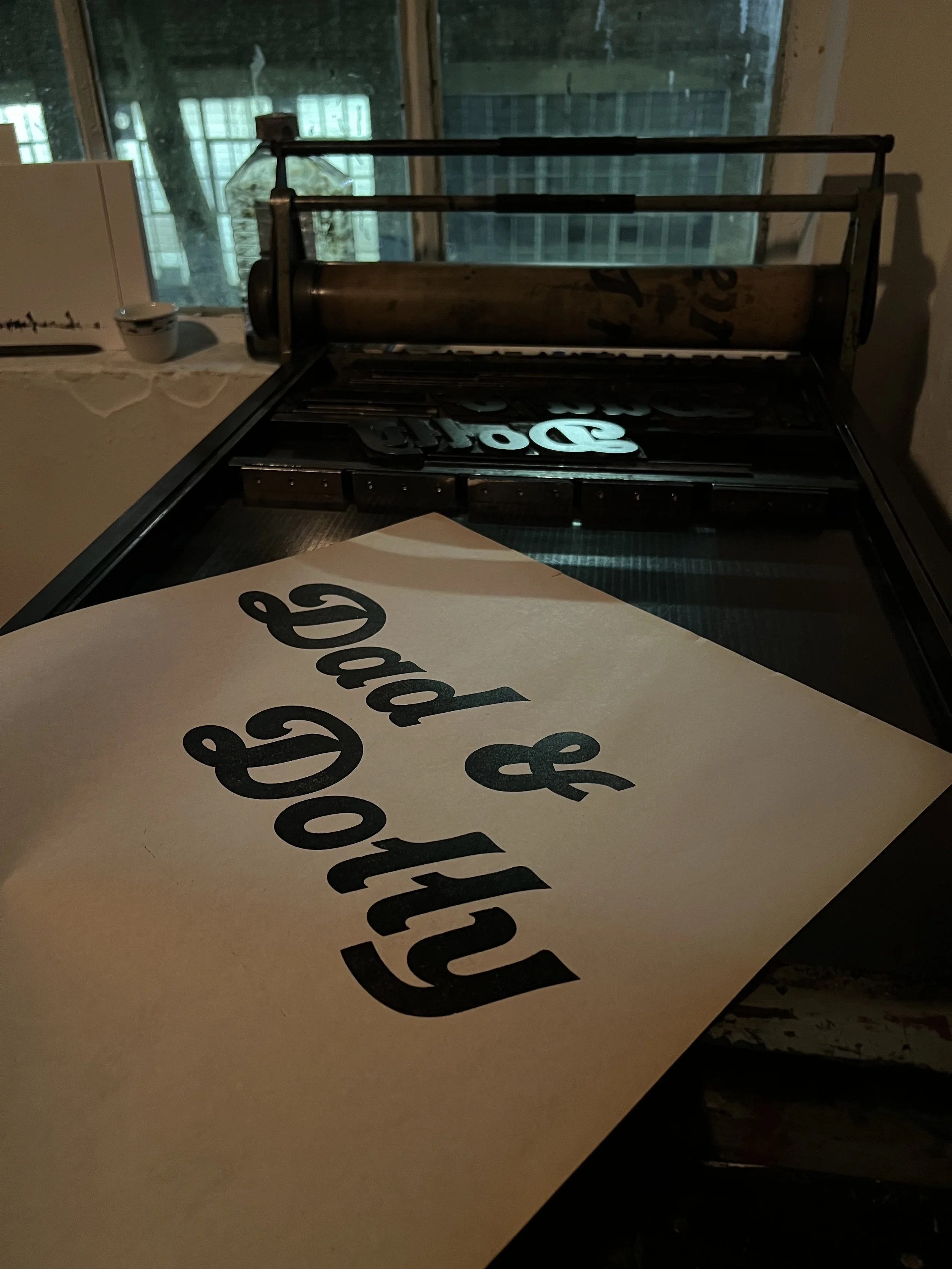 A close-up of a cardboard pizza box with the words 'food & drink' printed in large black letters. The background shows a window with a view of the outdoors and a coffee mug on a windowsill.