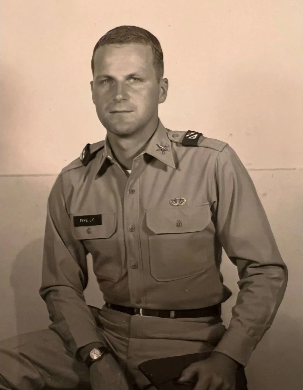 Black and white photo of a man in a military uniform sitting against a plain wall.