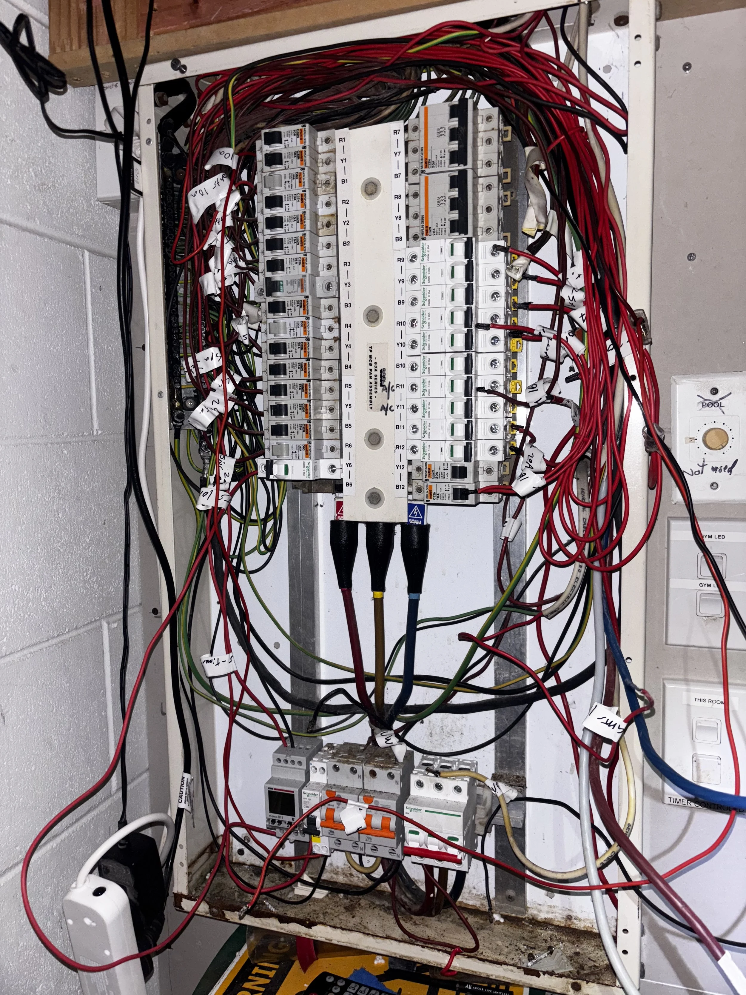 Electrical panel with numerous wires, circuit breakers, and electrical components inside a wall.