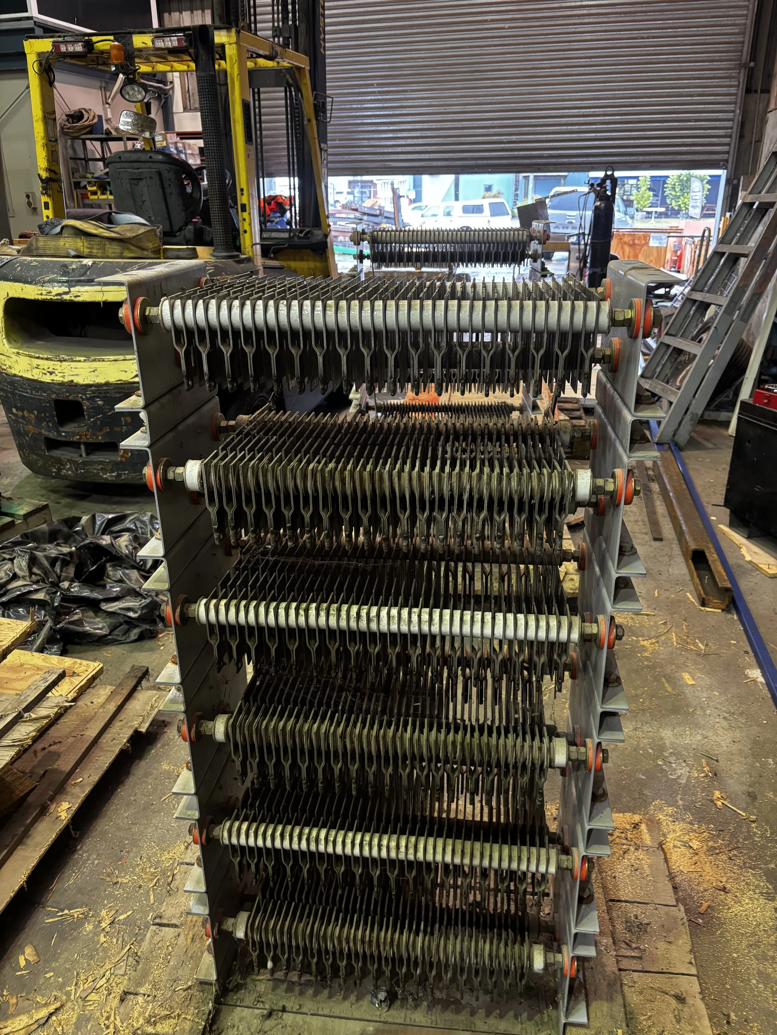 Stack of metal cooling or heating plates with bolts and rods in an industrial workshop.