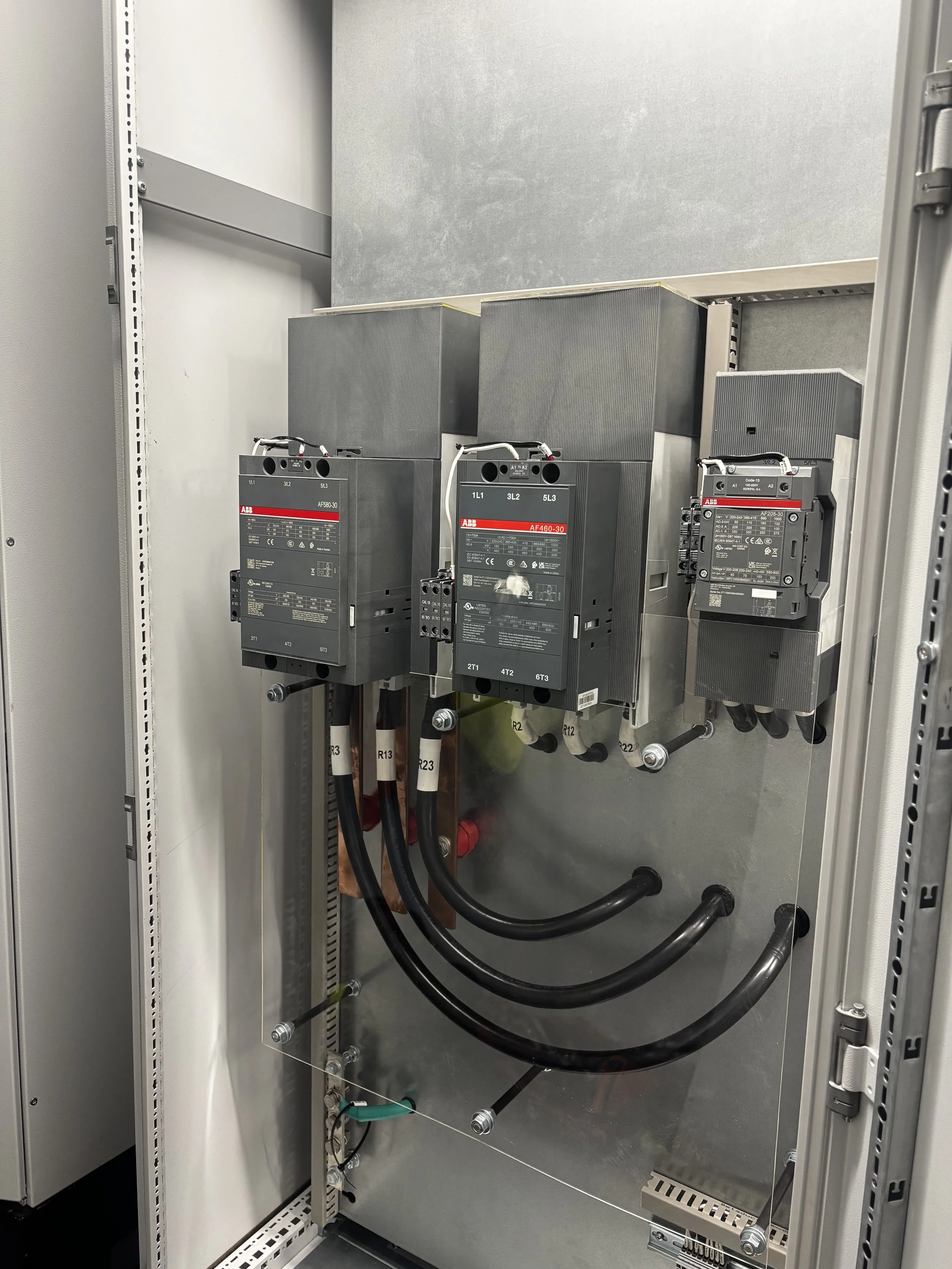 Electrical control panel with large circuit breakers, connected thick black cables, and metal mounting inside a gray metal enclosure.