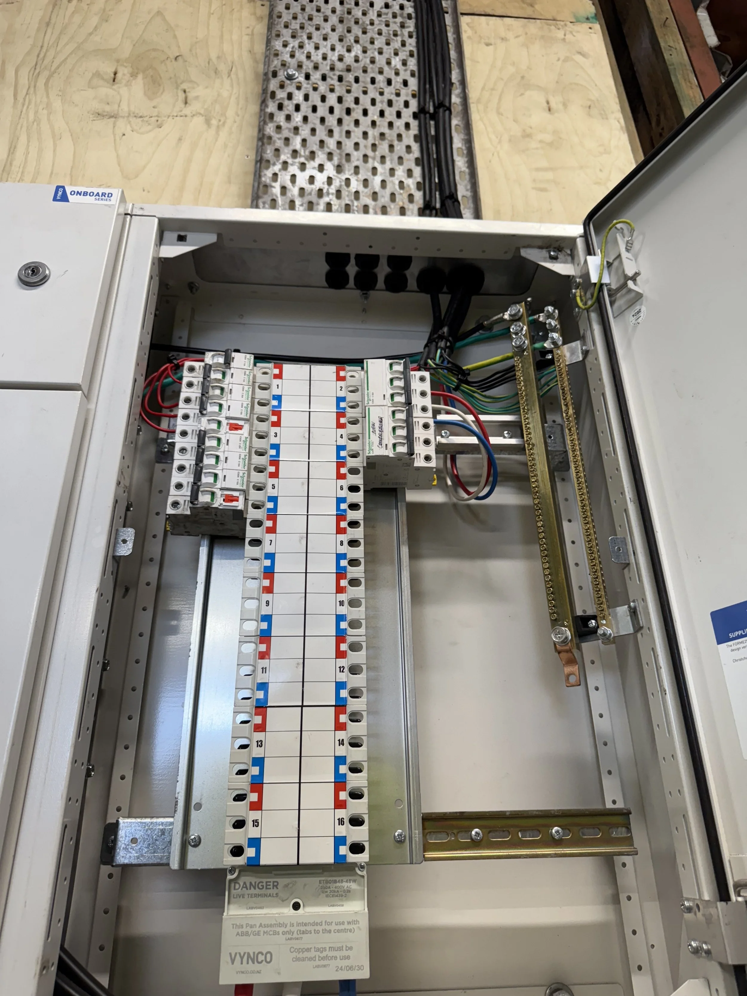 Open electrical control panel with wiring, circuit breakers, and a numbered relay rack on a wooden work surface.