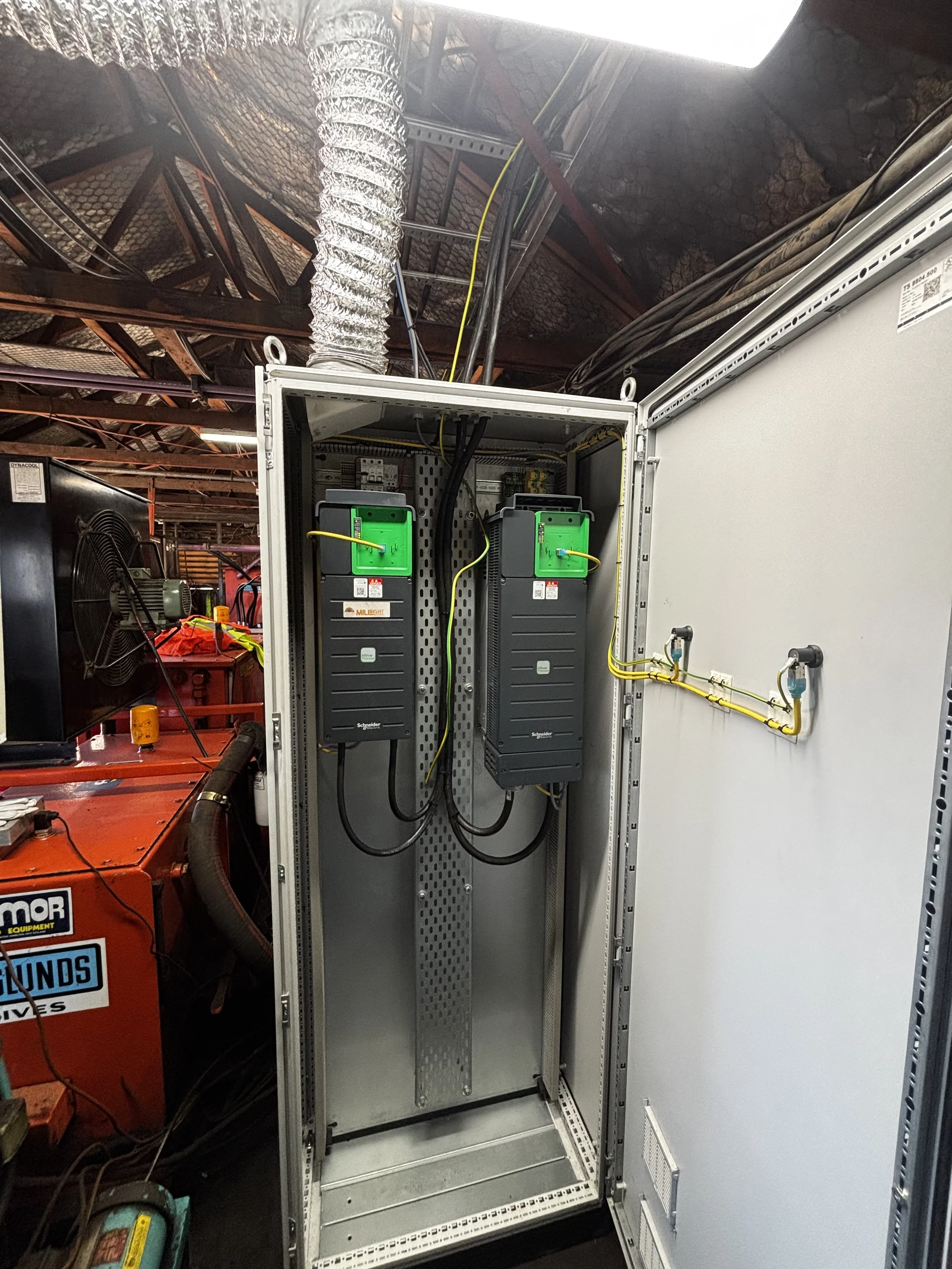 Electrical control cabinet with two blackgreen devices and yellow and black cables inside an industrial setting.