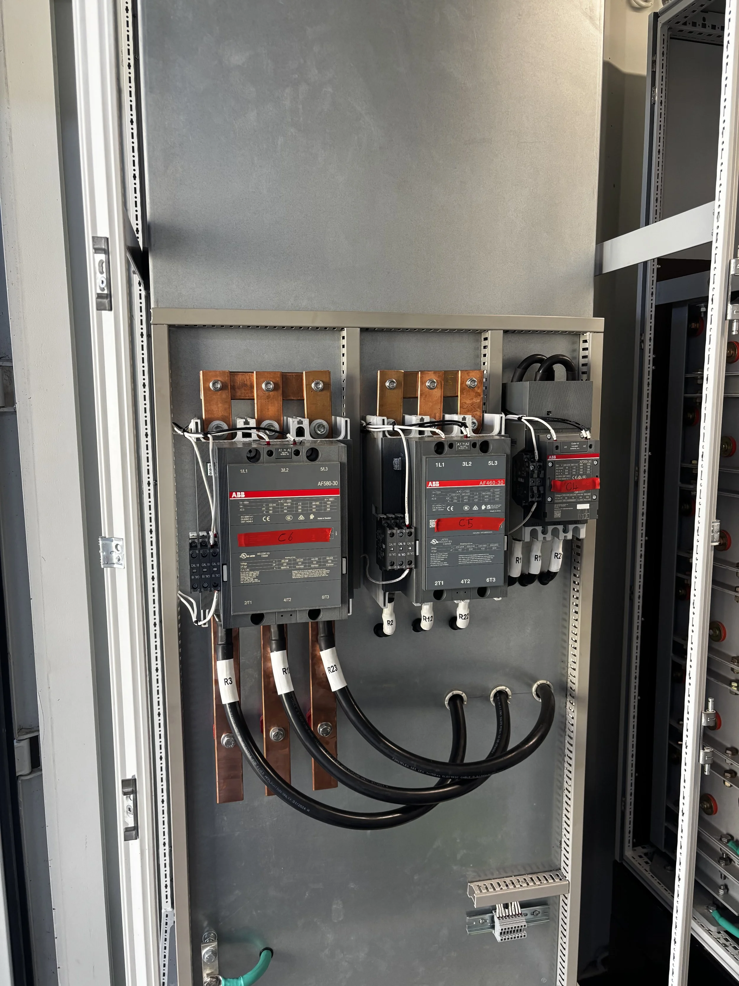 Electrical control panel with three large circuit breakers, copper bus bars, and connected thick black cables.