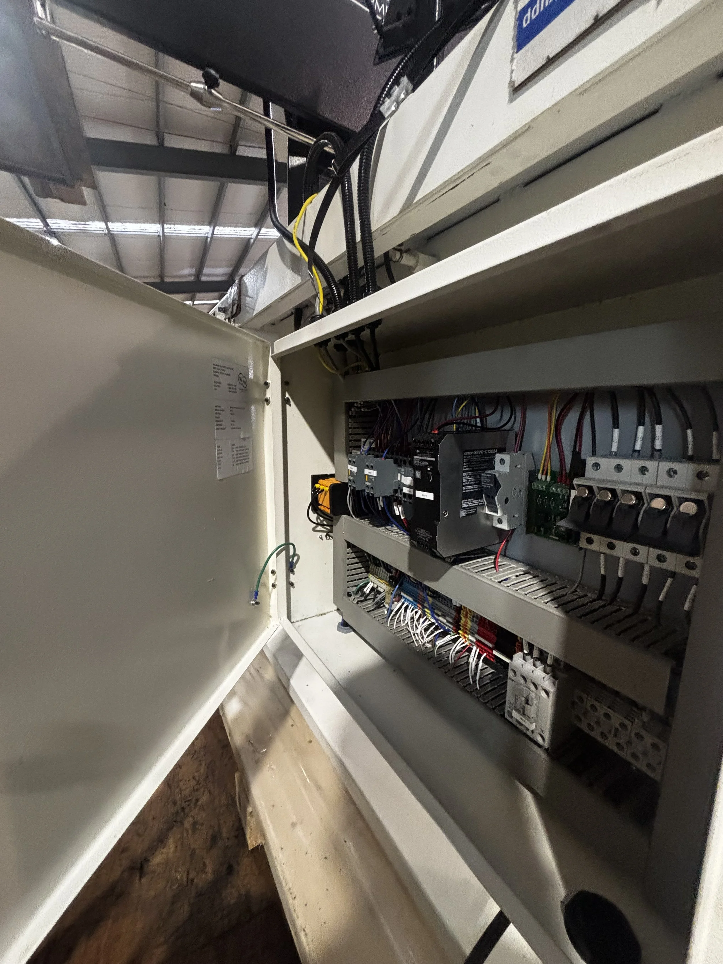 Open electrical control panel with various wires, circuit boards, and switches inside a white metal box.