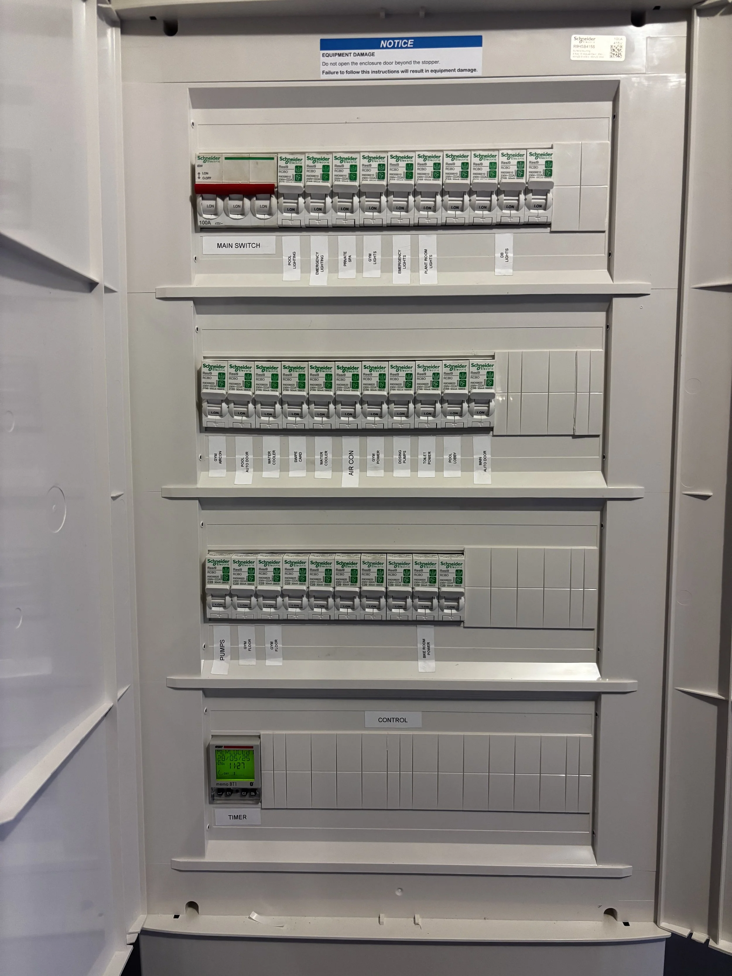 An electrical panel with multiple circuit breakers labeled with various electrical circuits; includes a small digital timer at the bottom left.