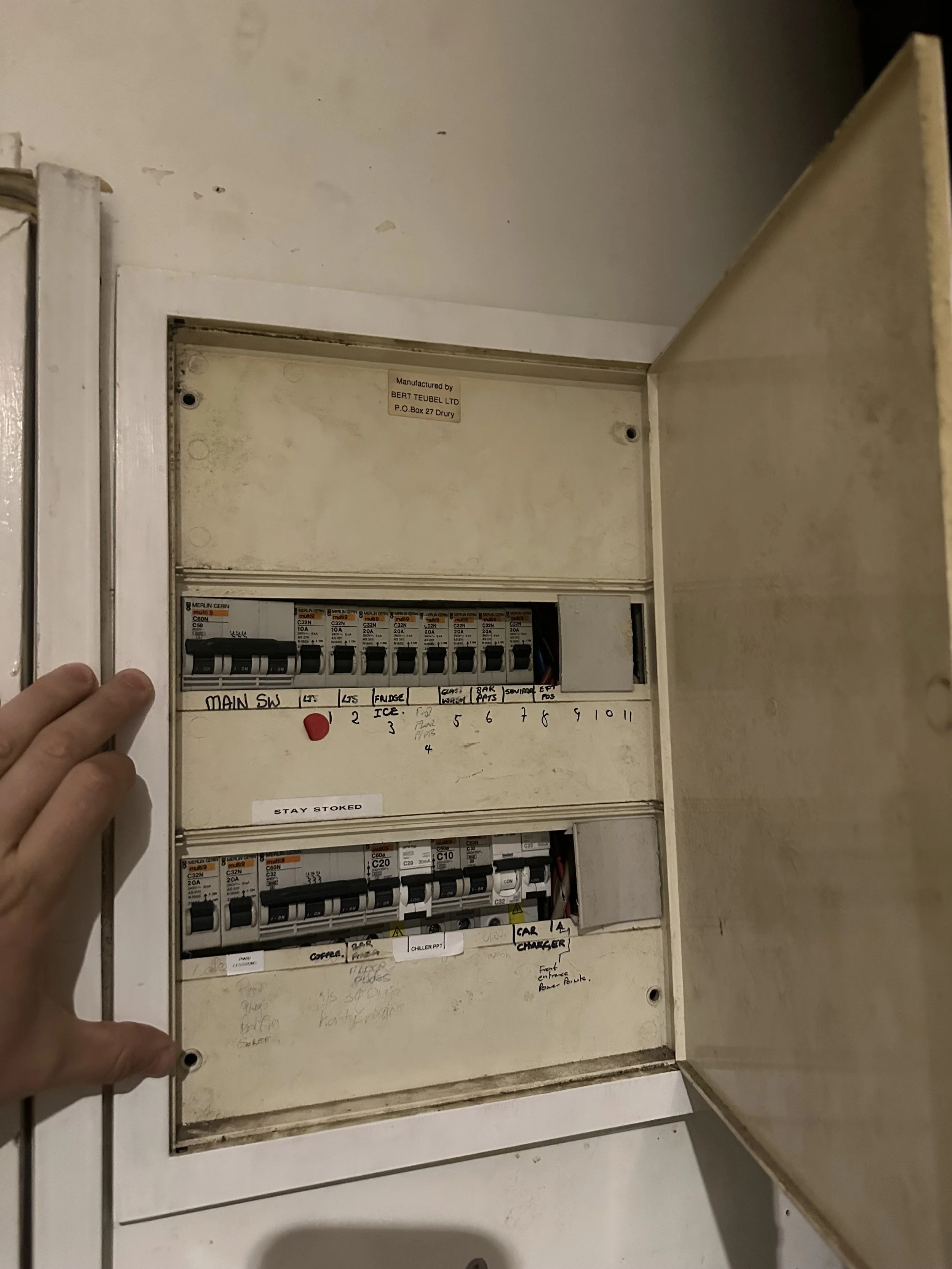 Open electrical breaker box with labeled switches and handwritten notes inside.
