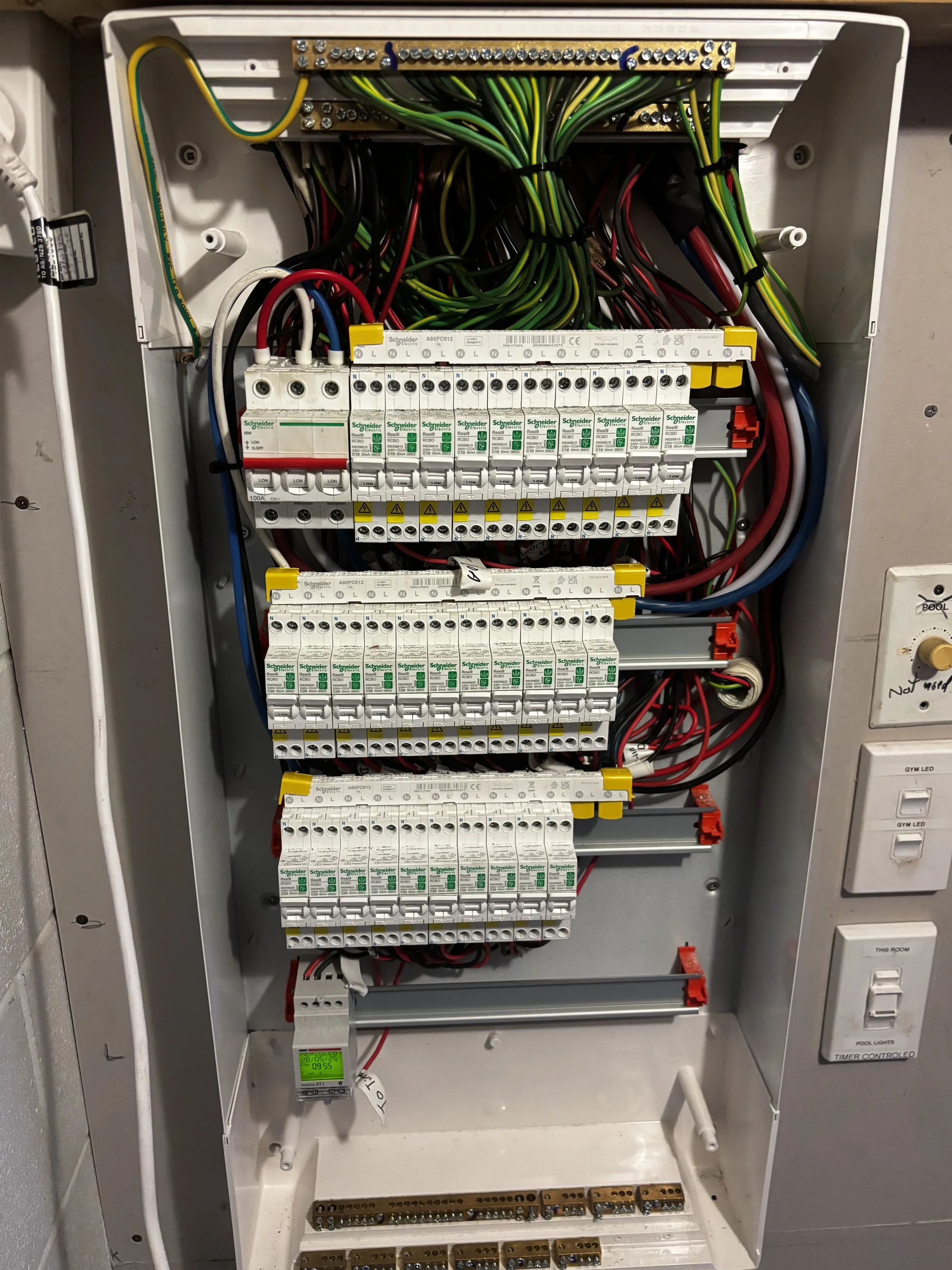 An open electrical panel containing multiple circuit breakers, wiring, and a digital meter, with switches and labels on the side.