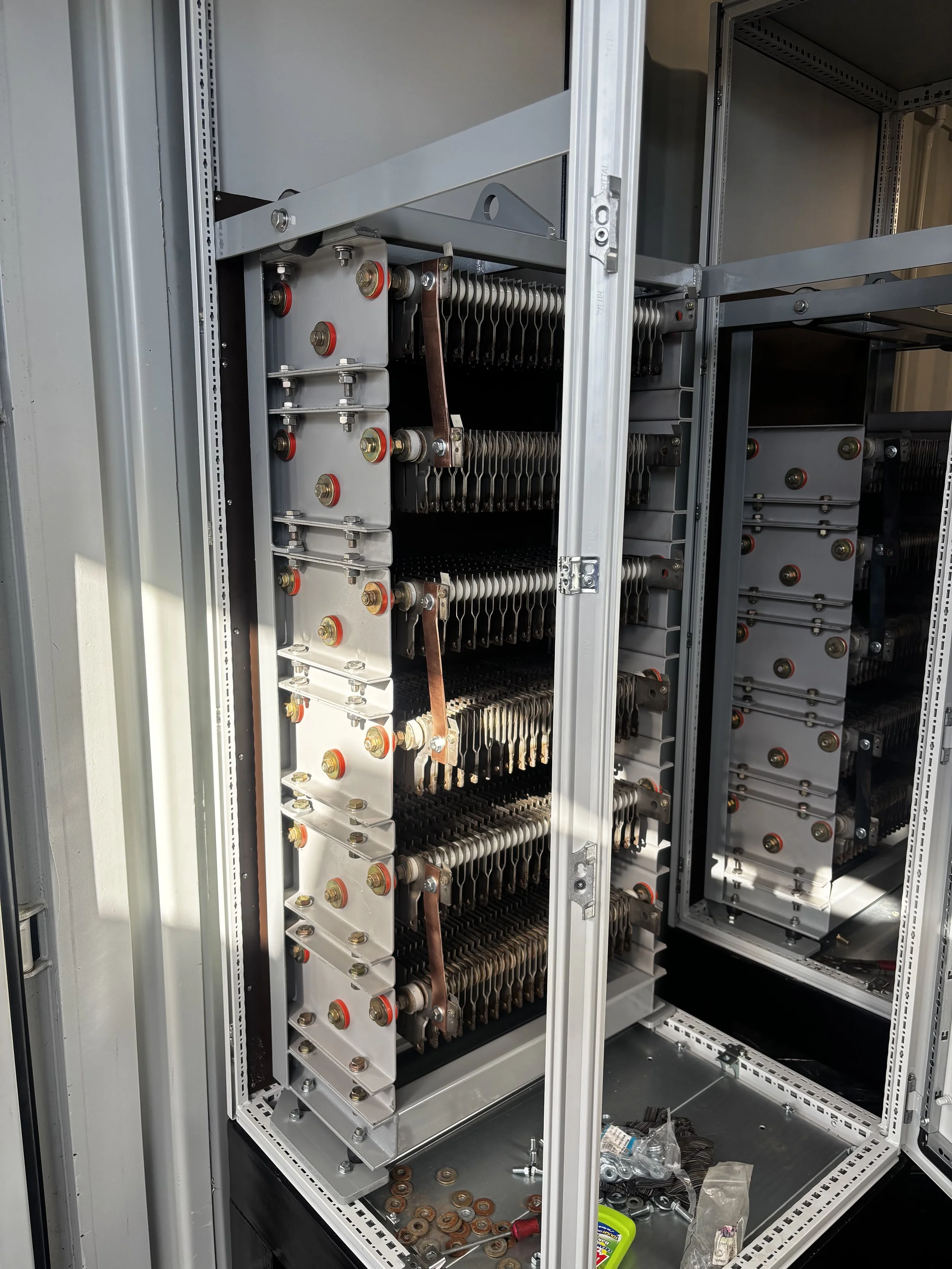 Close-up of an open electrical control panel with large metal components, connectors, and wiring, some tools and small parts inside the panel.