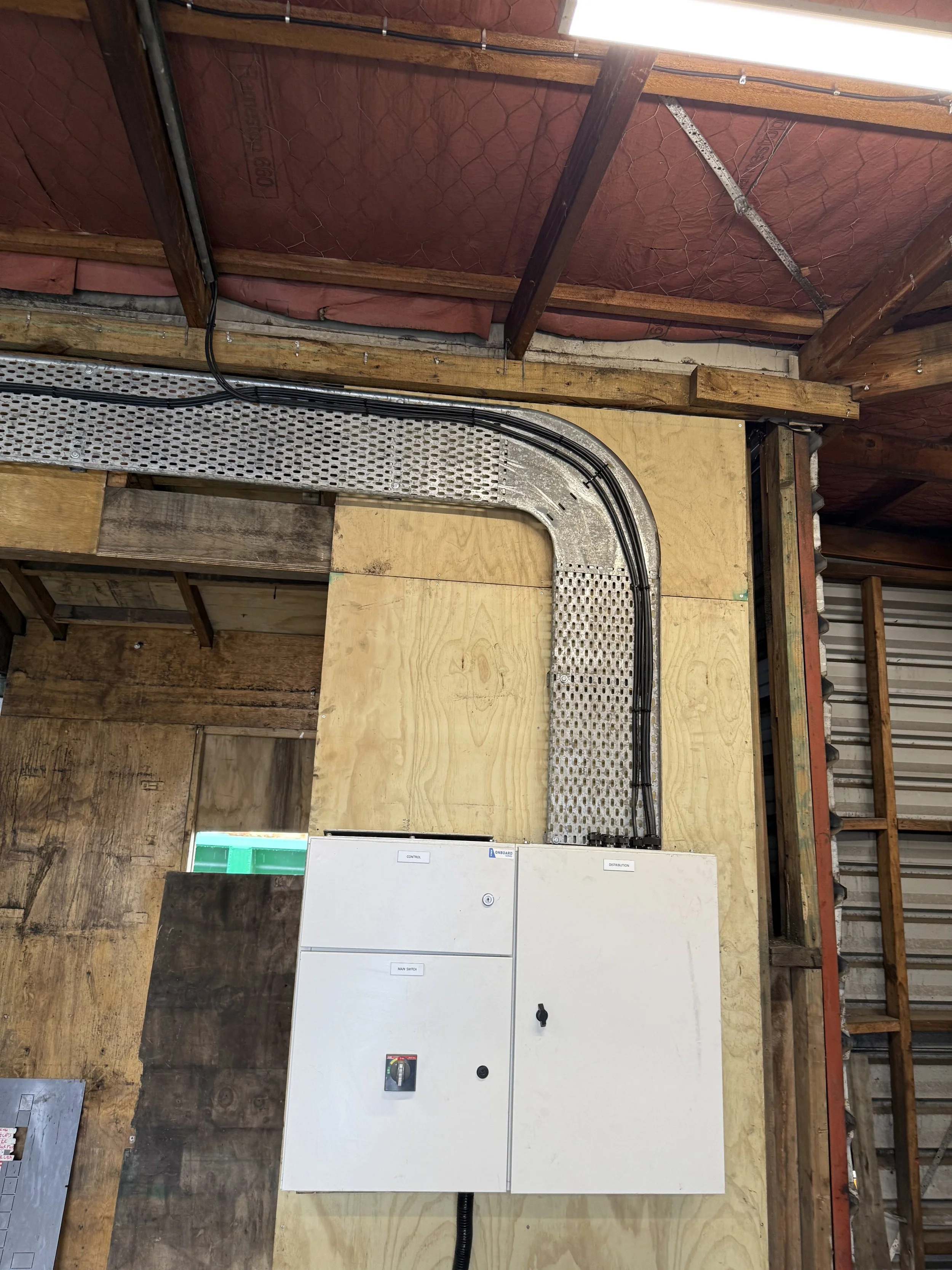 Electrical control panel with wiring and conduits mounted on a wooden wall in a construction setting.