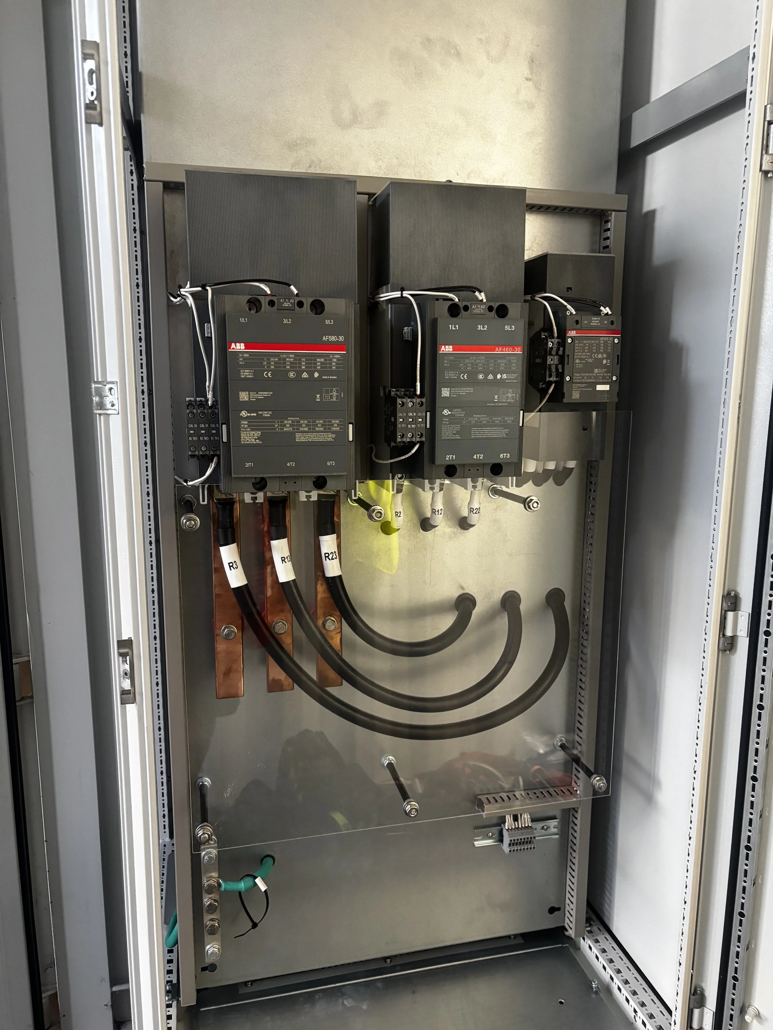 Electrical panel with three large ABB circuit breakers, copper and black cables connected to the breakers, mounted inside a metal enclosure.