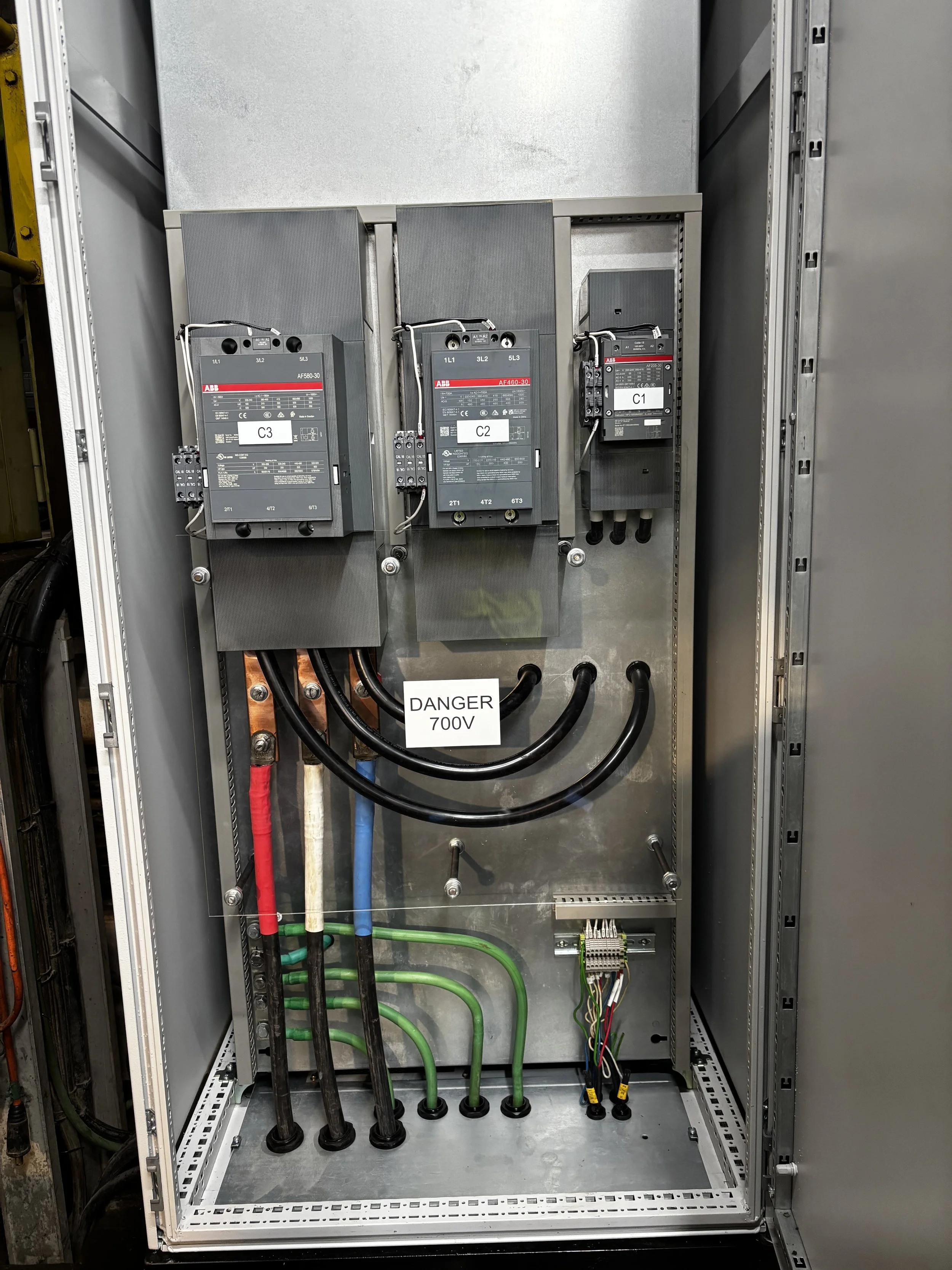 Electrical panel with three large circuit breakers labeled C1, C2, and C3, wiring connections, and a warning sign indicating 700V.