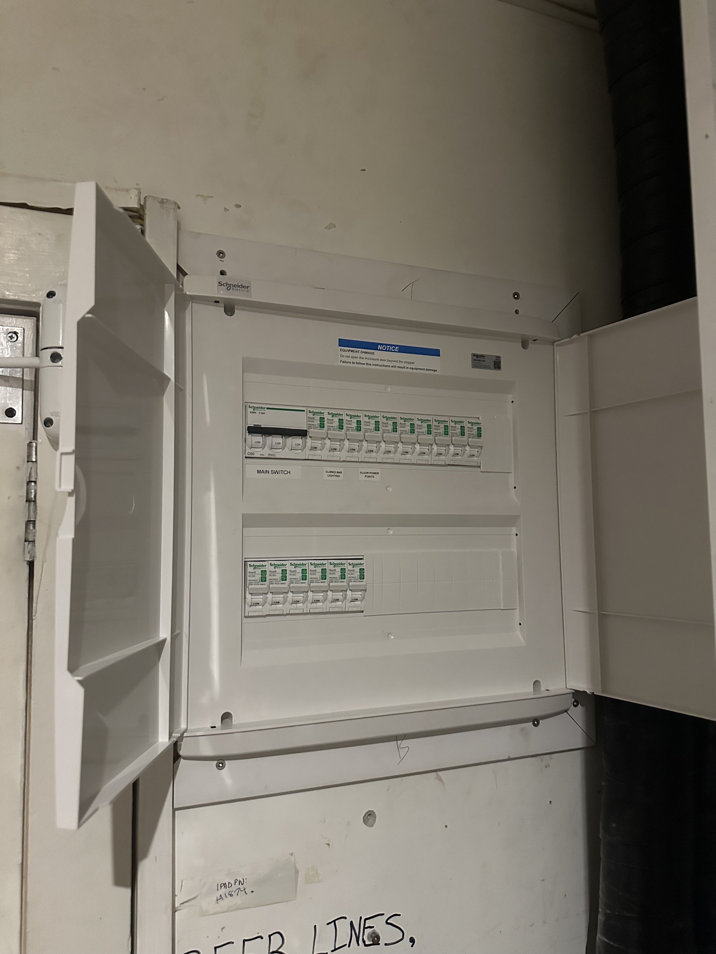 Electrical breaker panel with open cover showing circuit breakers, labeled main switch, mounted on a wall.