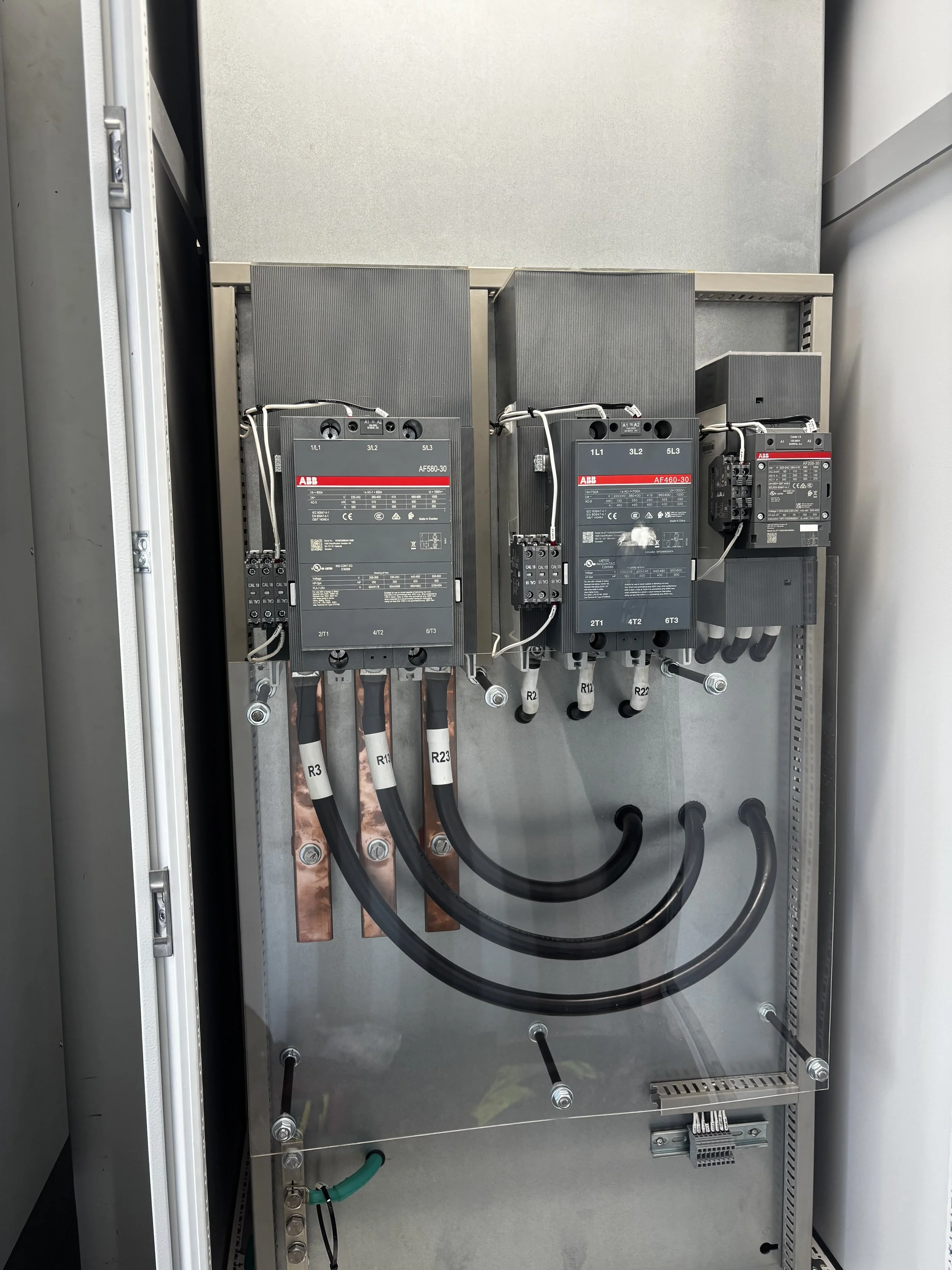 Electrical control panel with two large black ABB drives, wiring, and cables mounted inside a metal enclosure.