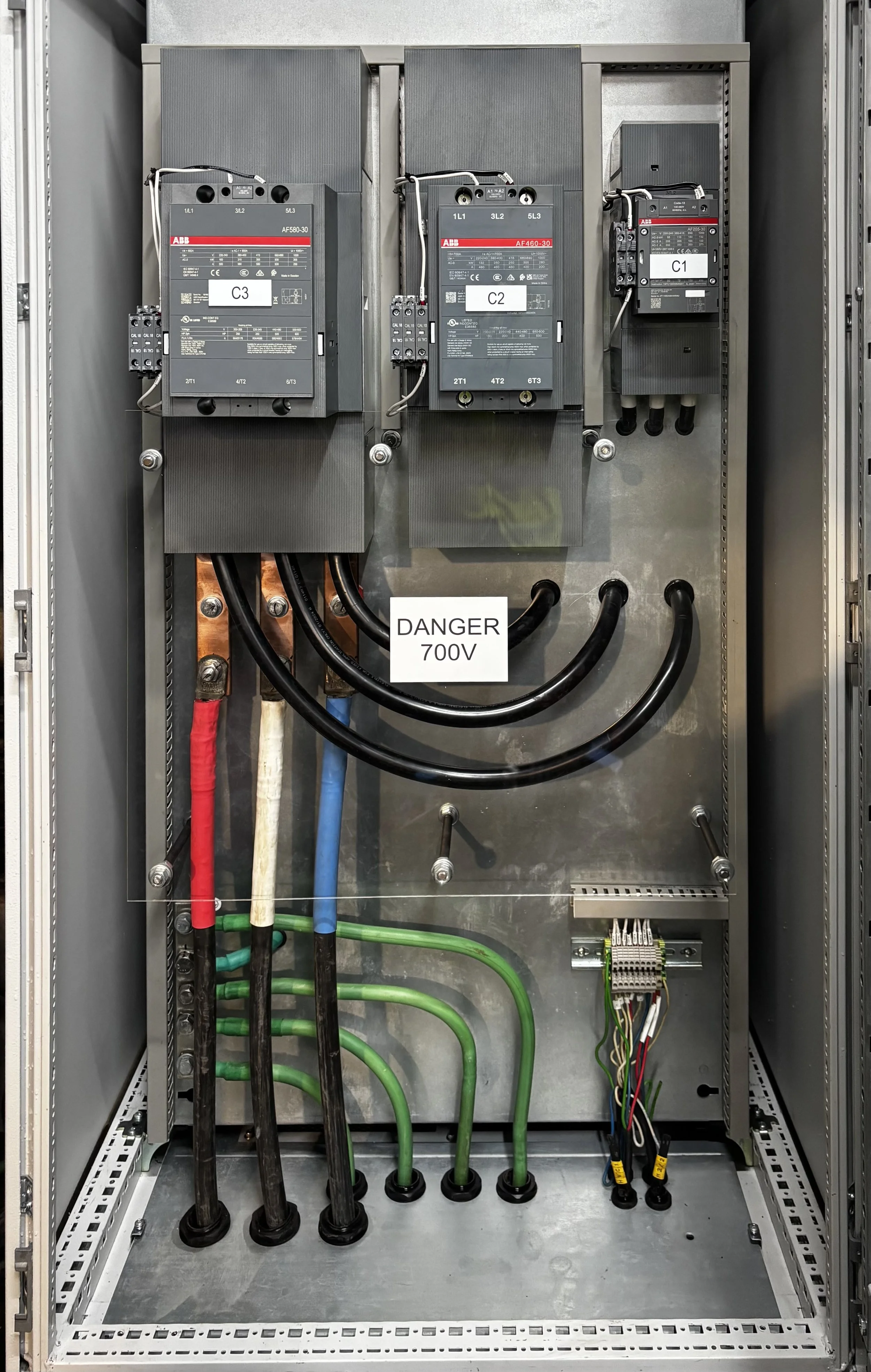 Electrical panel with three large circuit breakers, wiring, and a warning sign reading 'DANGER 700V'.