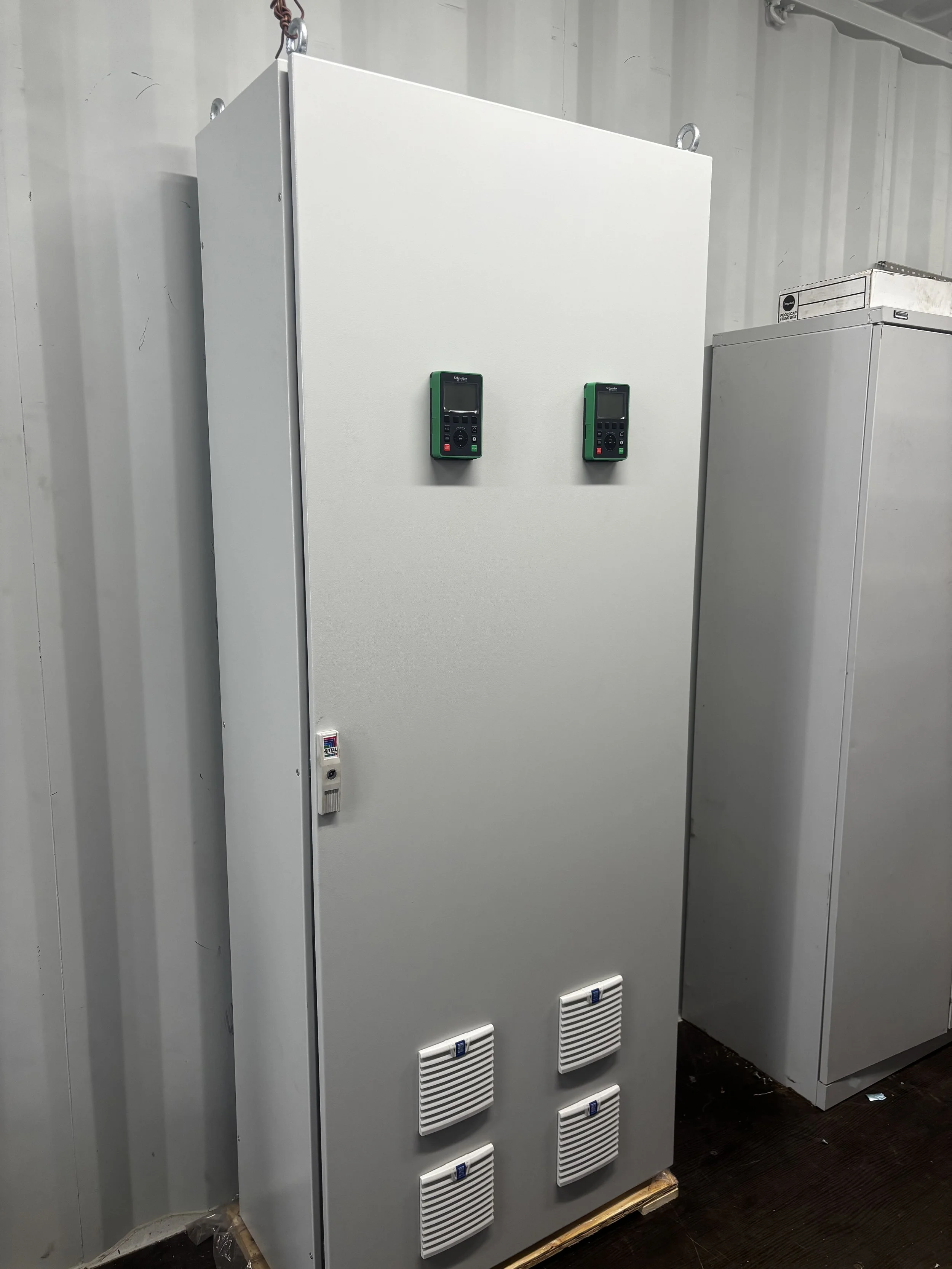 Electrical equipment cabinet with two handheld devices attached to the front and four ventilation vents at the bottom.