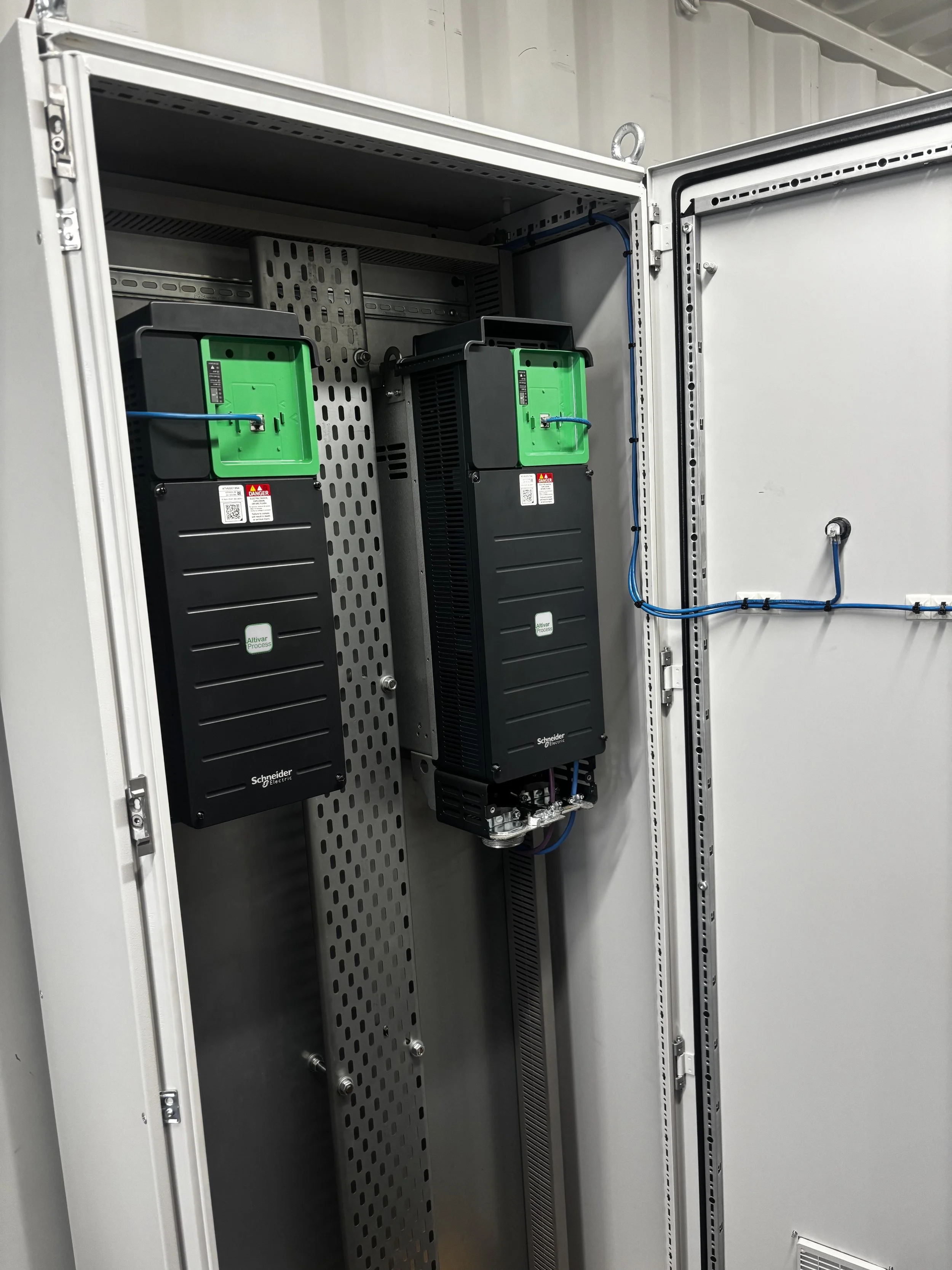 Inside an electrical cabinet with two Schneider Electric Altivar Process variable frequency drives mounted on a metal backplane, with wiring connected.