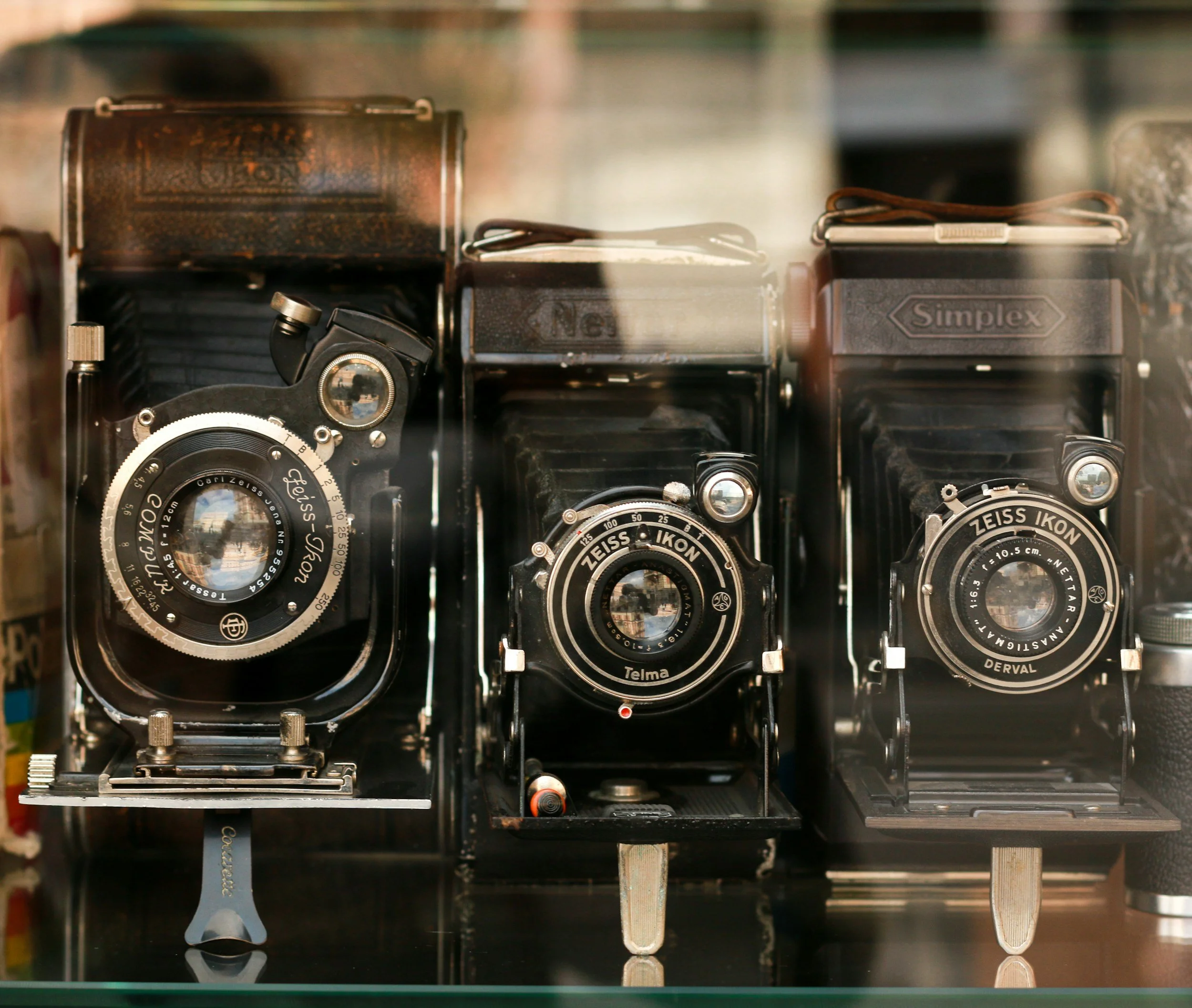 Three vintage large-format view cameras with black bellows and lenses displayed behind glass.