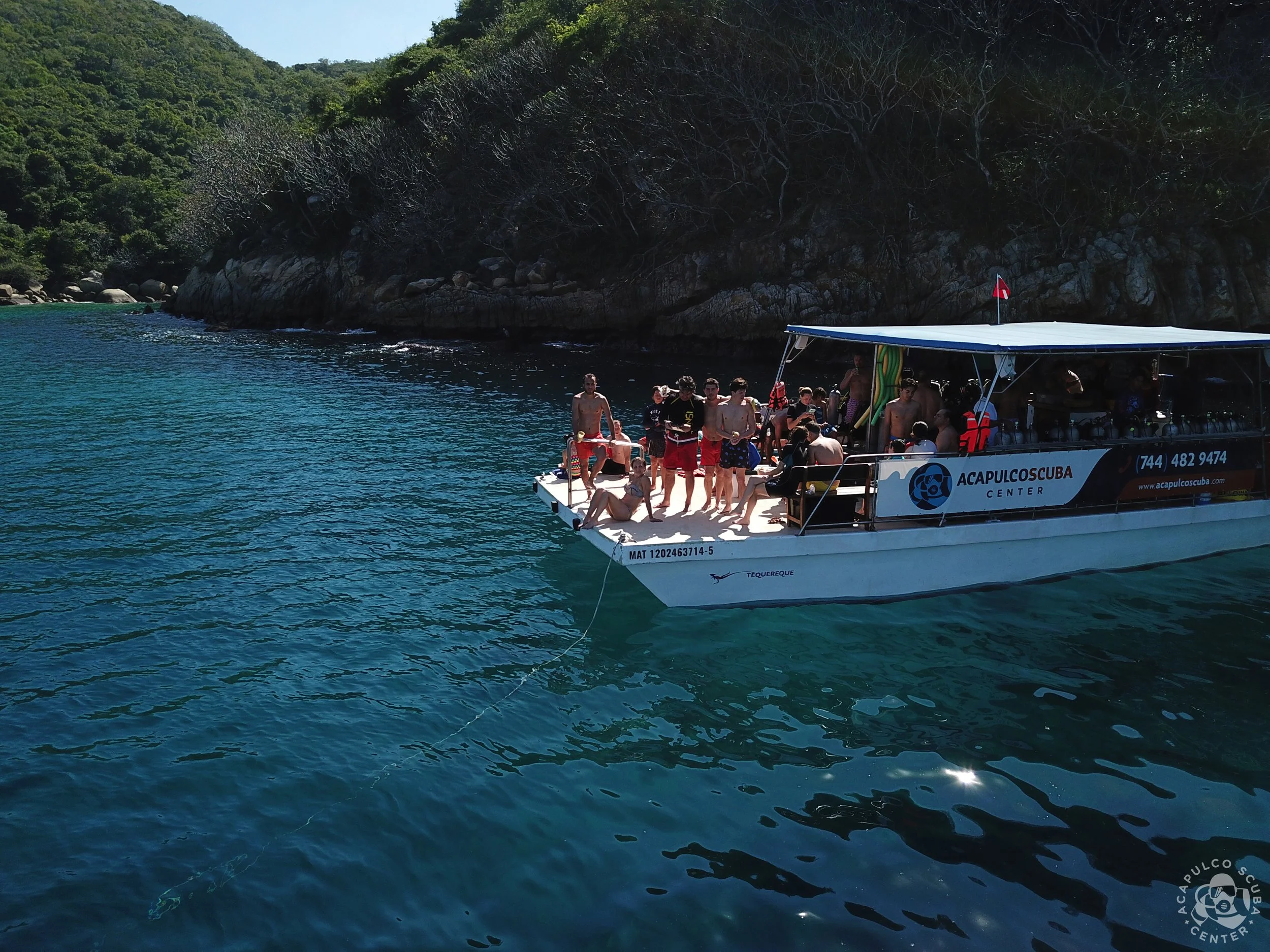 A group of people on a boat in a clear blue sea with forested hills in the background.