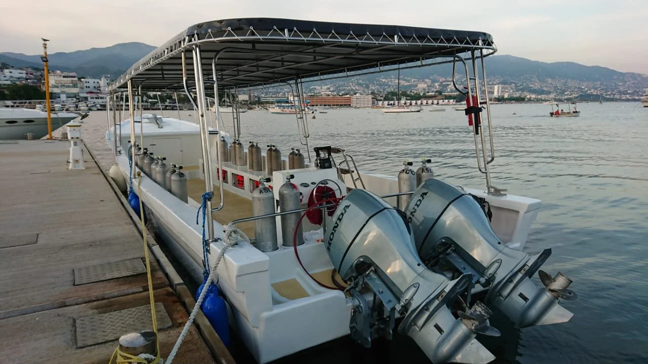 A white boat docked at a marina with two Honda outboard engines and Olympic grade scuba tanks onboard.