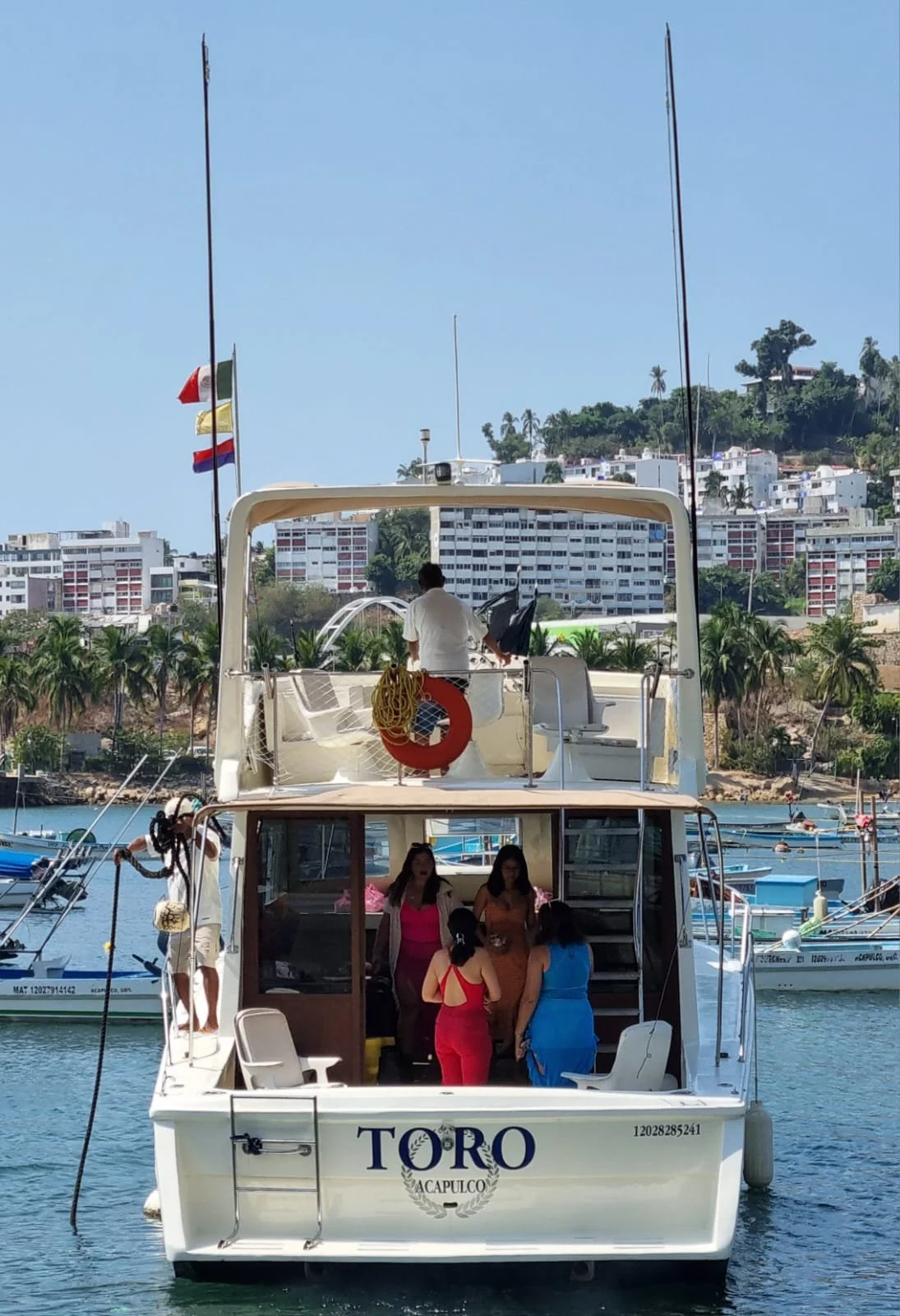 A boat named 'Toro' on the water with people on deck, and a cityscape with buildings and palm trees in the background.