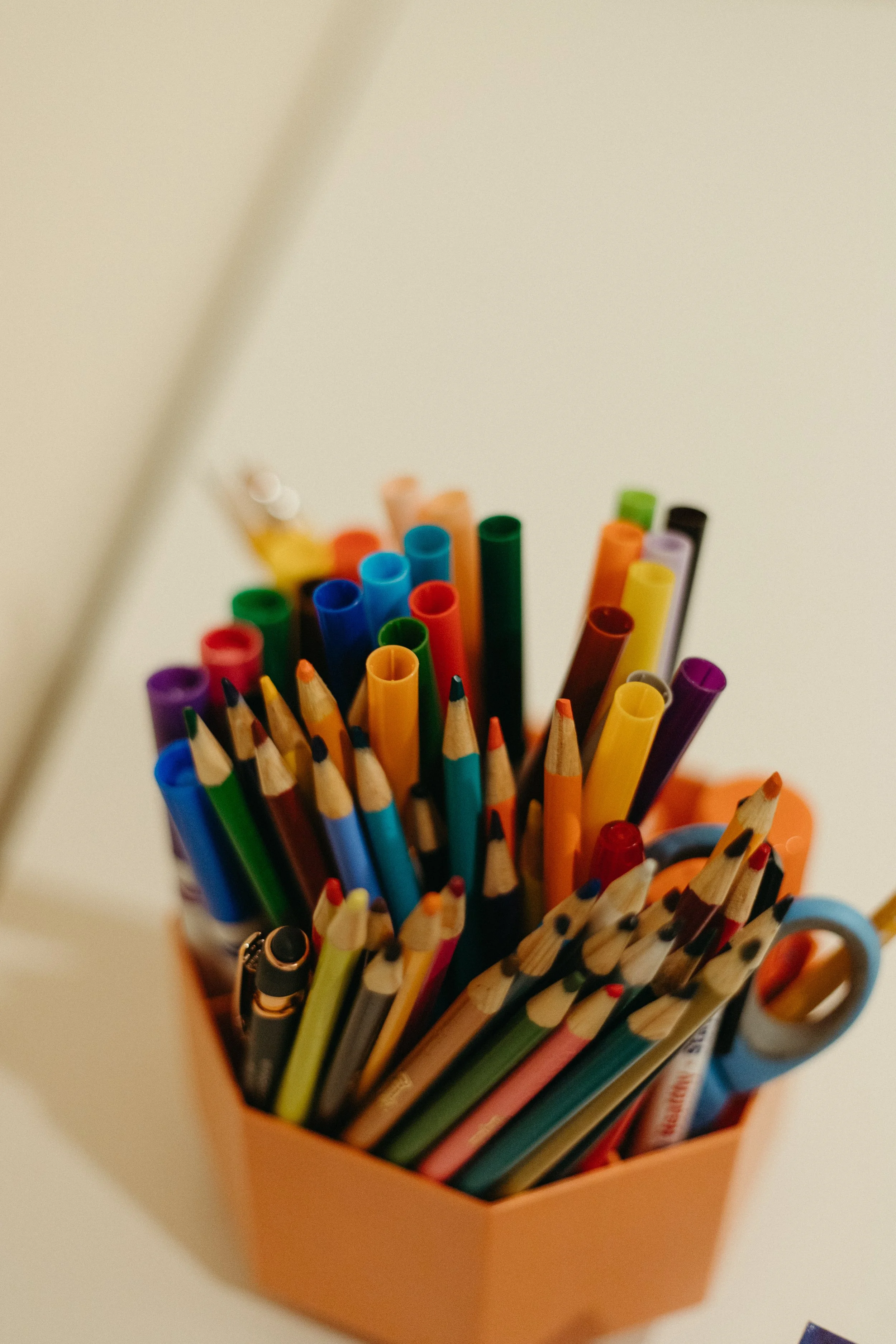 A collection of colored pencils, markers, and pens organized in an orange container on a white surface.