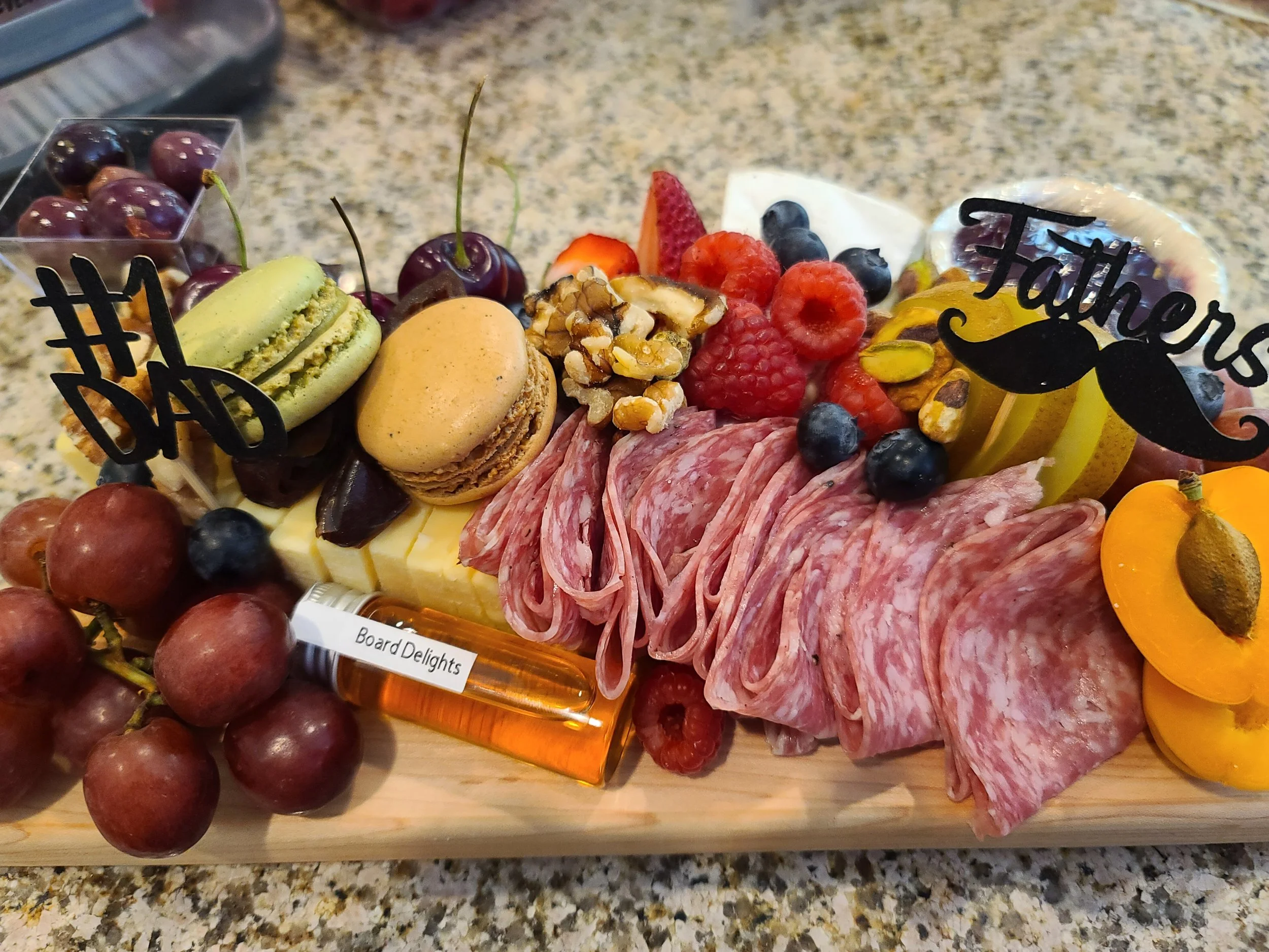 Charcuterie board with salami, cheese, grapes, strawberries, raspberries, blueberries, nuts, macarons, and decorative signs reading 'Happy Dad' and 'Fathers'.